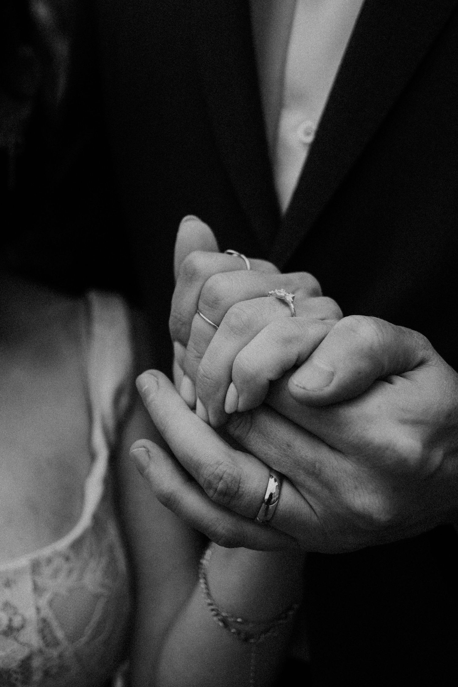 Black and white photo of a couple holding hands, showing wedding and engagement rings, symbolizing love and commitment.