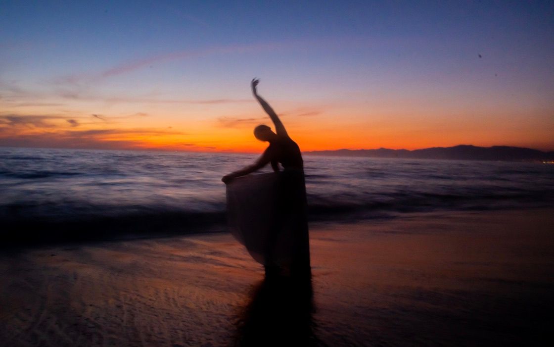 Silhouette stretching gracefully on beach shore during golden sunset.