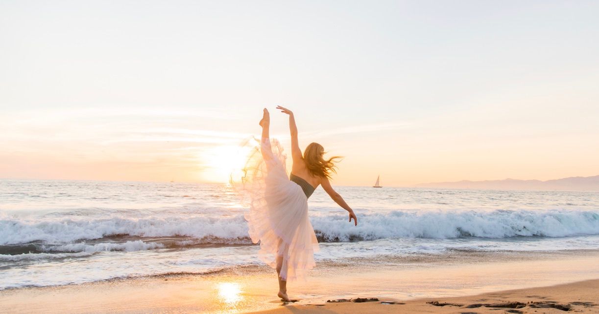 A graceful ballet pose performed on a beach during golden hour.