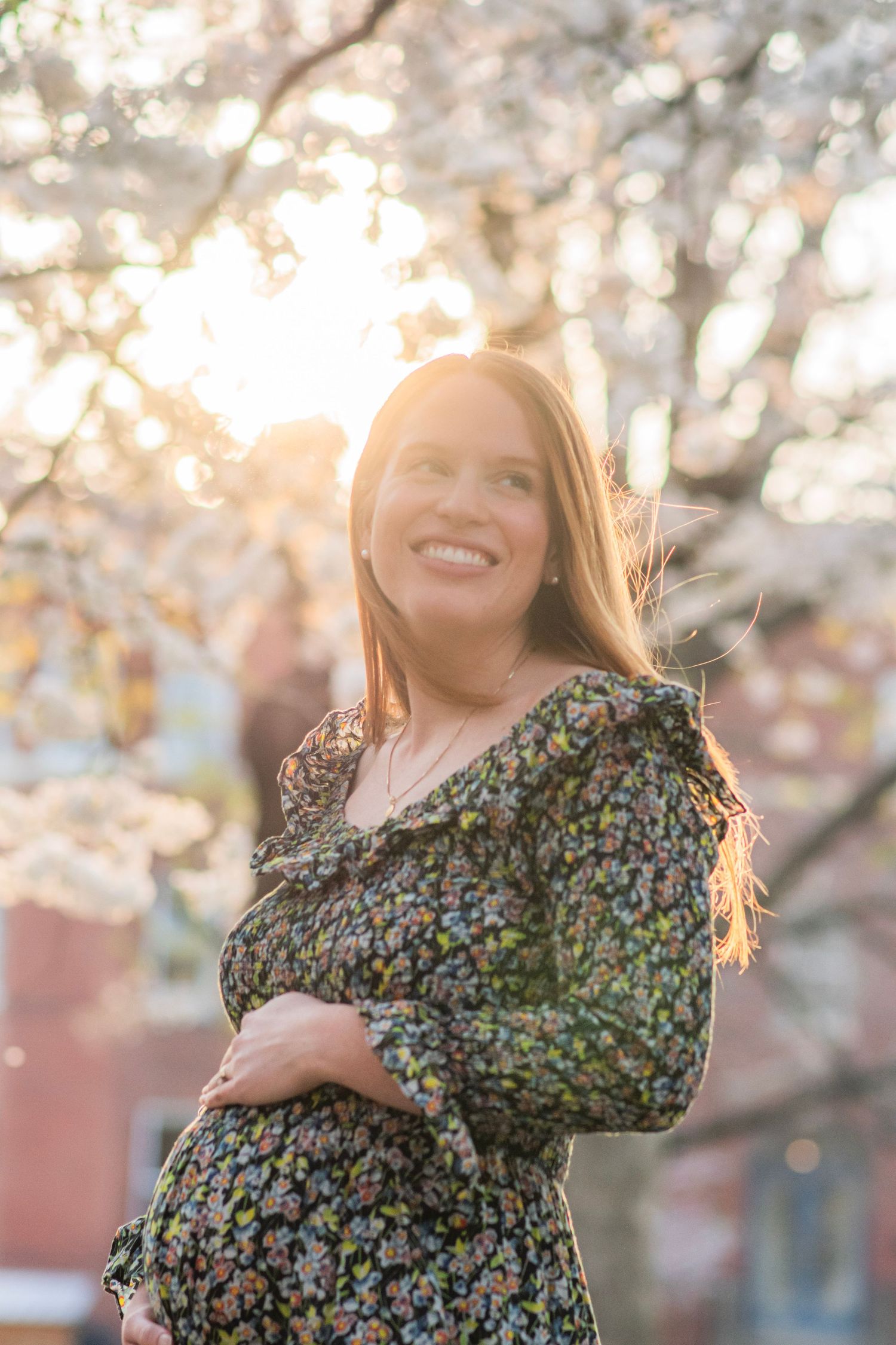 Sunlit spring portrait under cherry blossoms wearing a vintage-style floral dress.