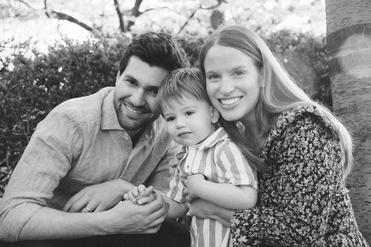 Black and white family portrait with toddler under cherry blossom trees.