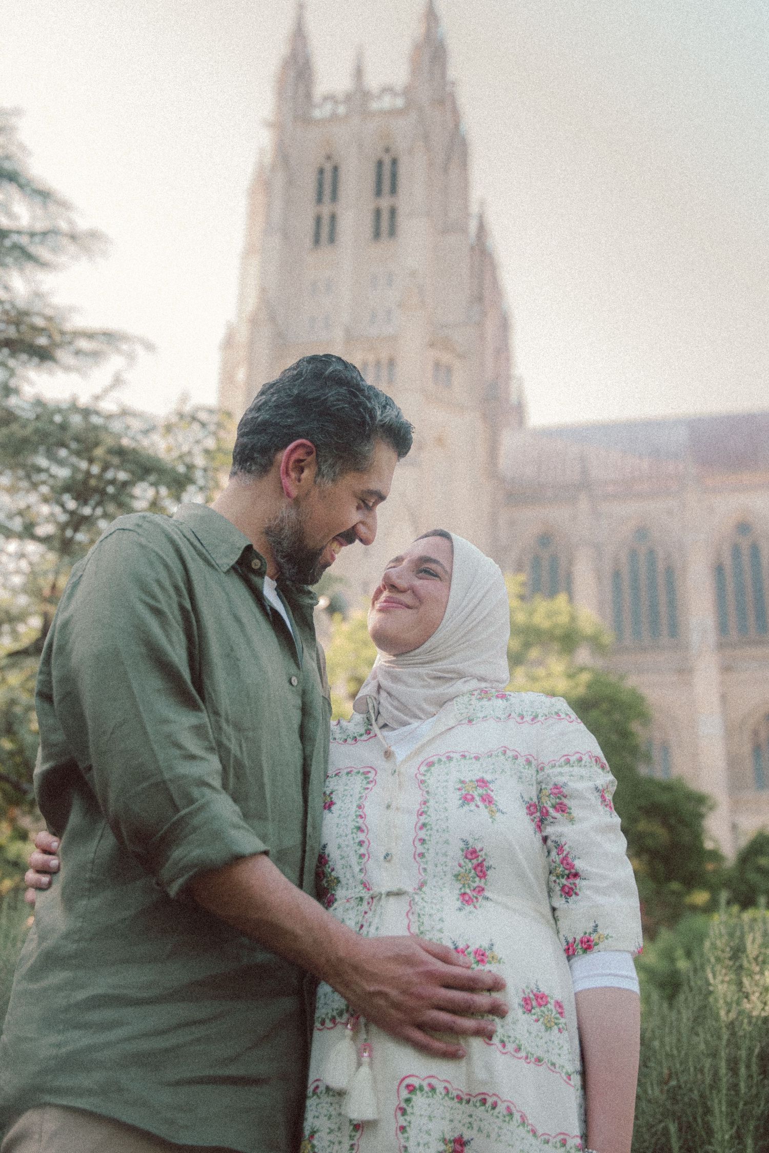 A couple embracing and smiling at each other in front of a historic stone tower building outdoors.