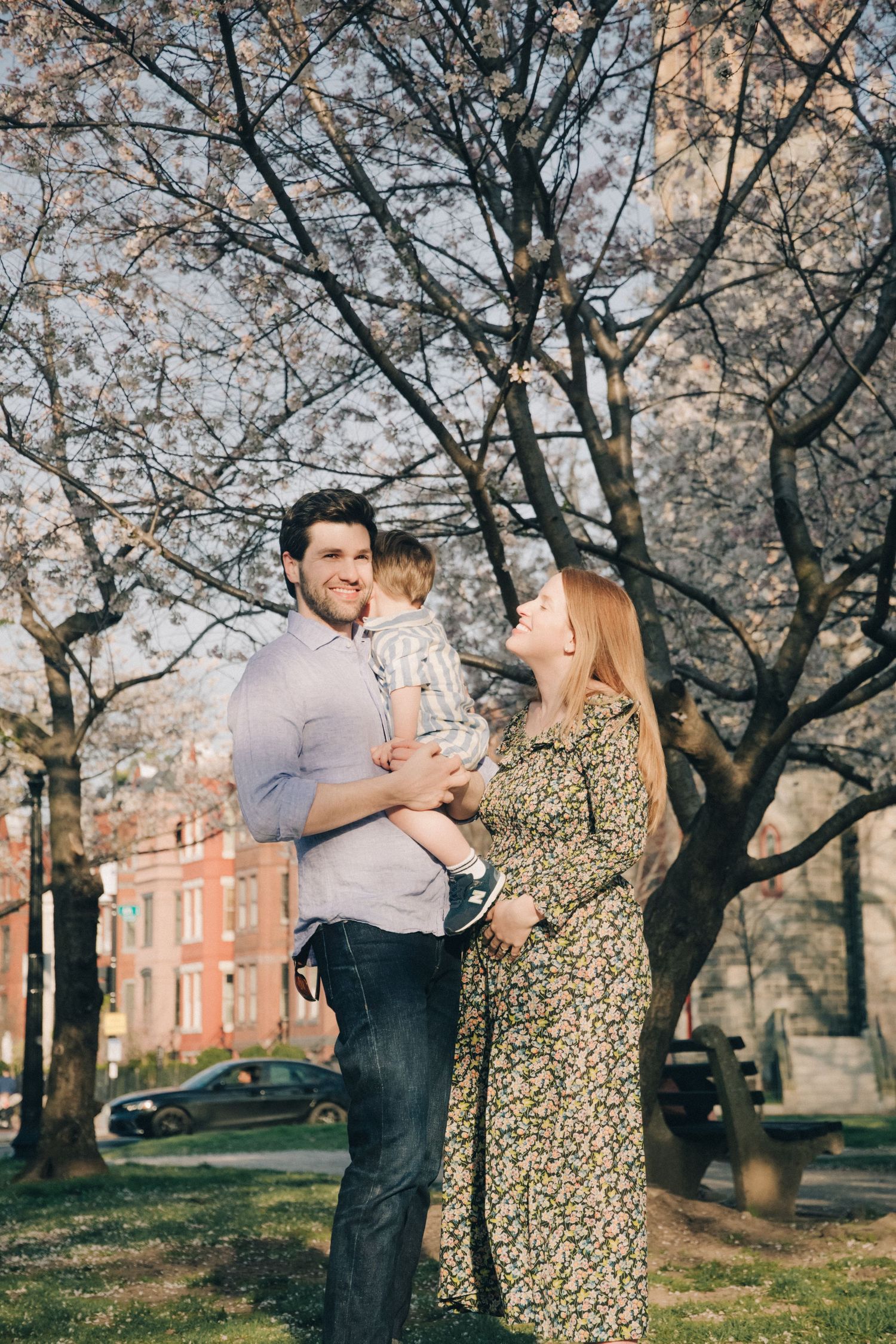 Family photo under cherry blossoms with toddler and expecting parents.