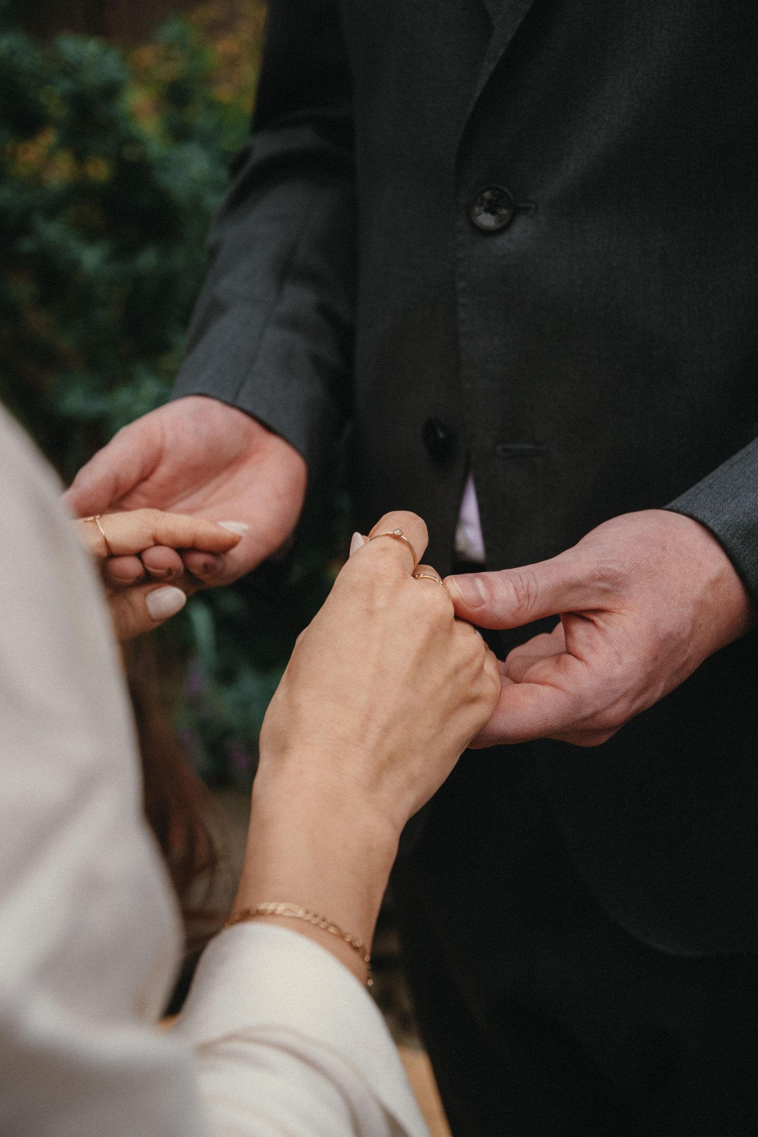 Bride placing a wedding ring on groom's finger during outdoor ceremony, close-up of hands exchanging rings.