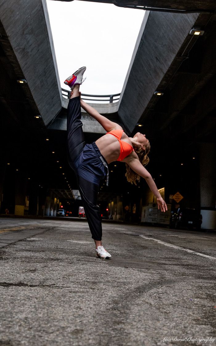 Athletic figure performs a dynamic breakdance move on concrete floor beneath an urban structure.