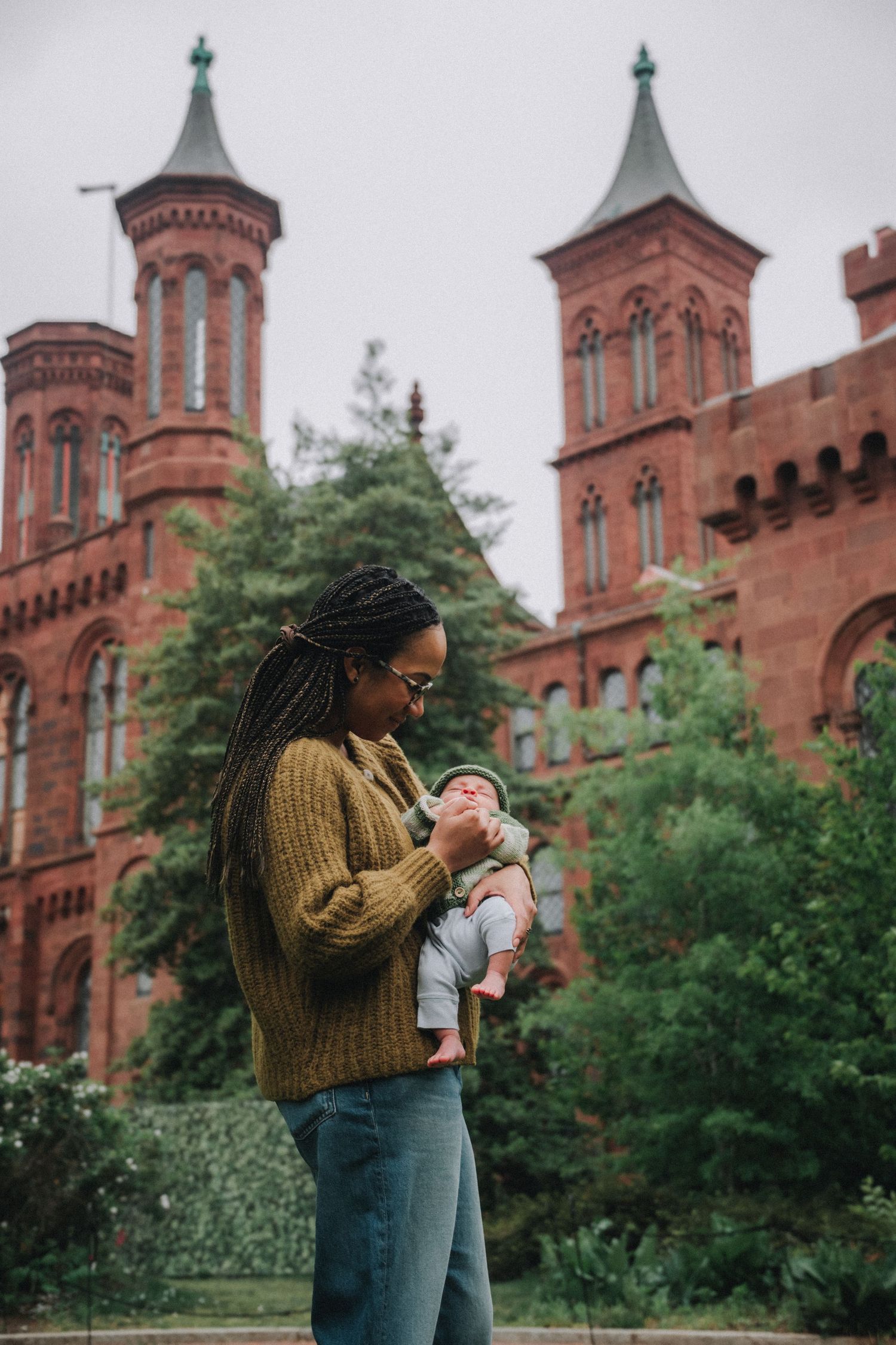 A woman holds her newborn baby outside the Smithsonian Castle in Washington D.C. on a cloudy day.