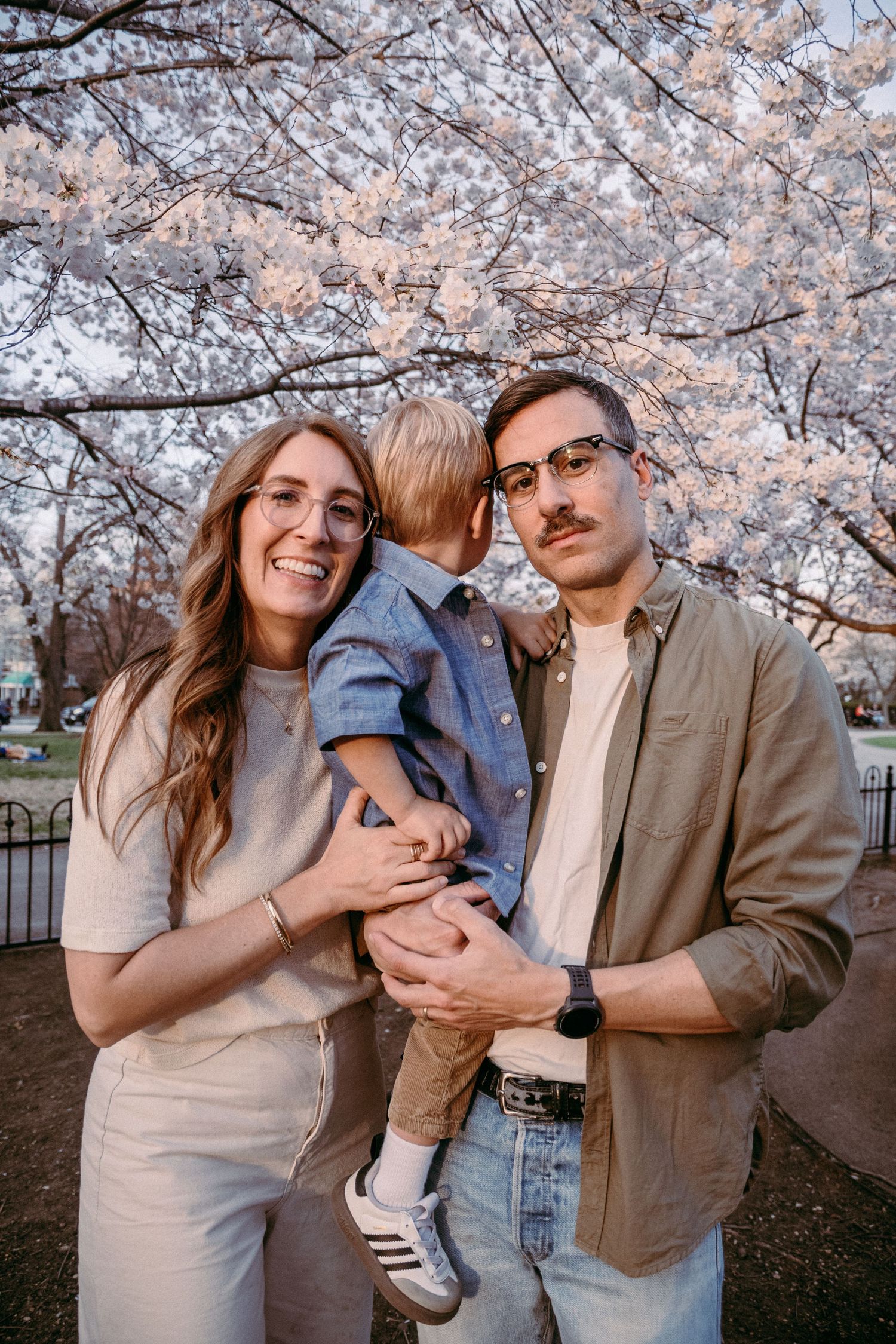 A family portrait beneath beautiful pink cherry blossoms on a spring day.
