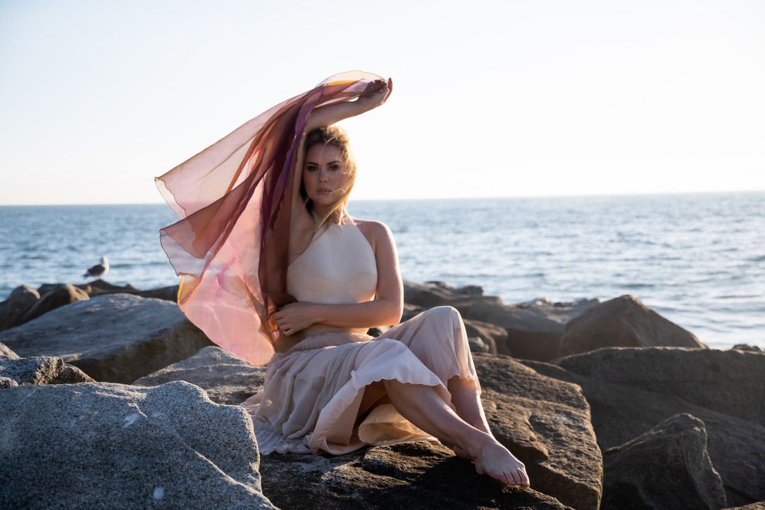 Artistic sunset photoshoot on rocky coastal beach with flowing fabric.