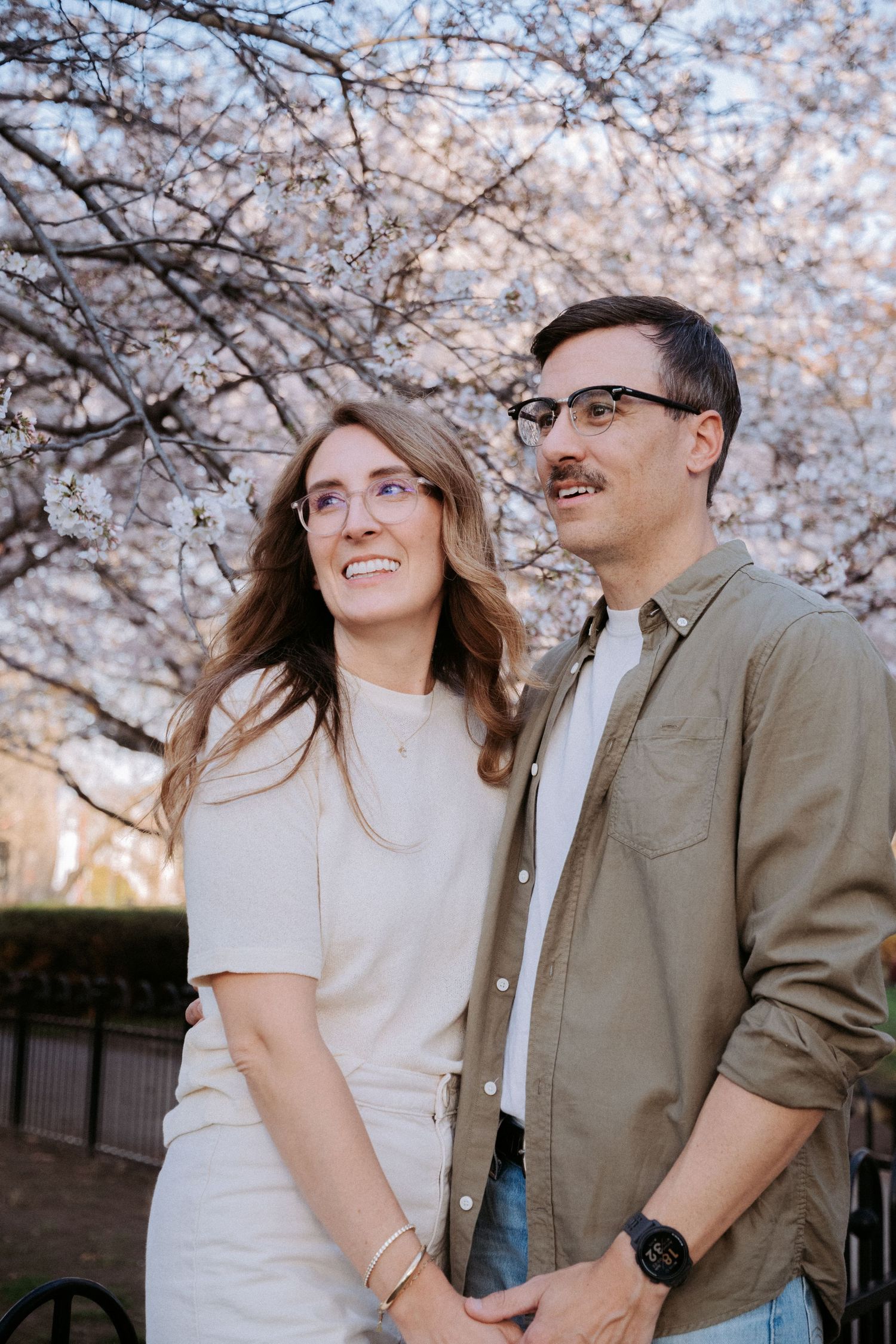 A springtime photo session beneath pink cherry blossoms with urban architecture visible.