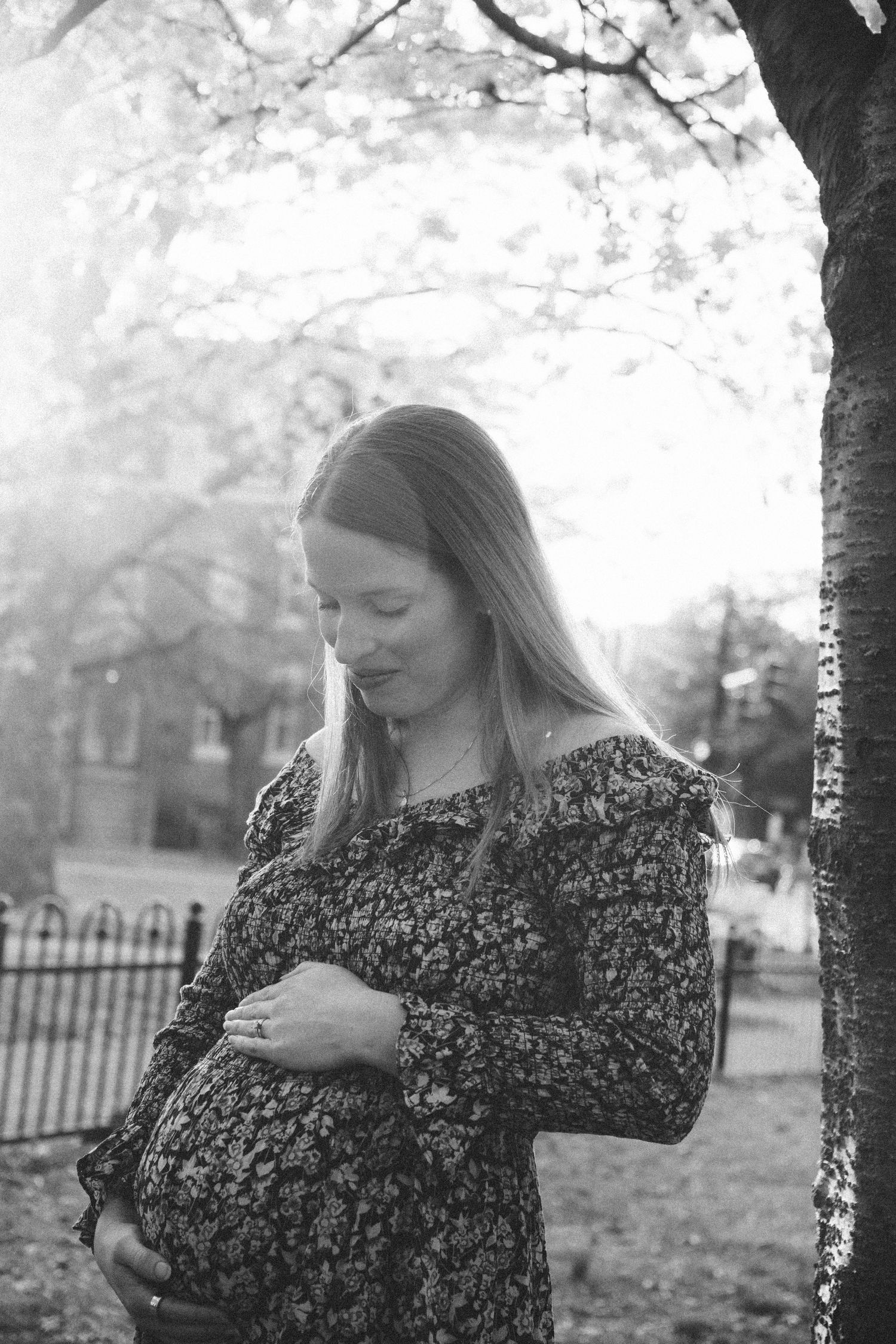 Black and white maternity photo under spring blossoms with soft lighting.