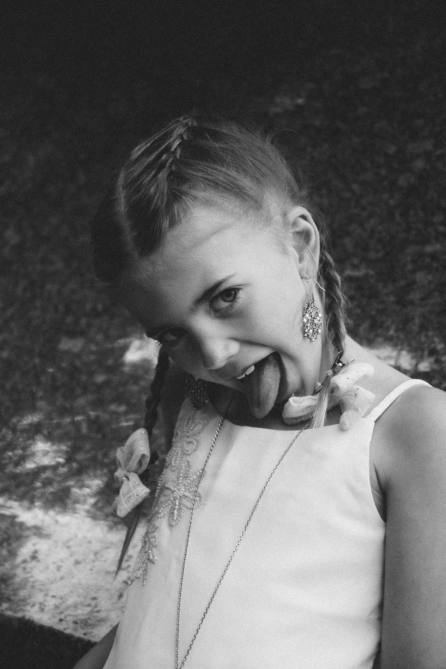 Black and white photo of a young girl with braids and earrings sticking out her tongue and smiling.