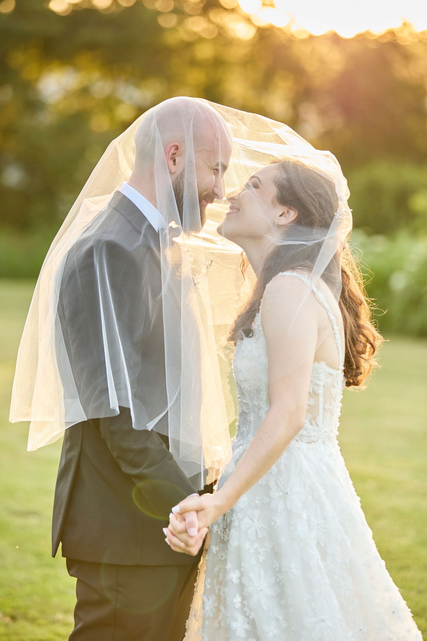 Bride and groom in golden hour sunset with veil over heads.