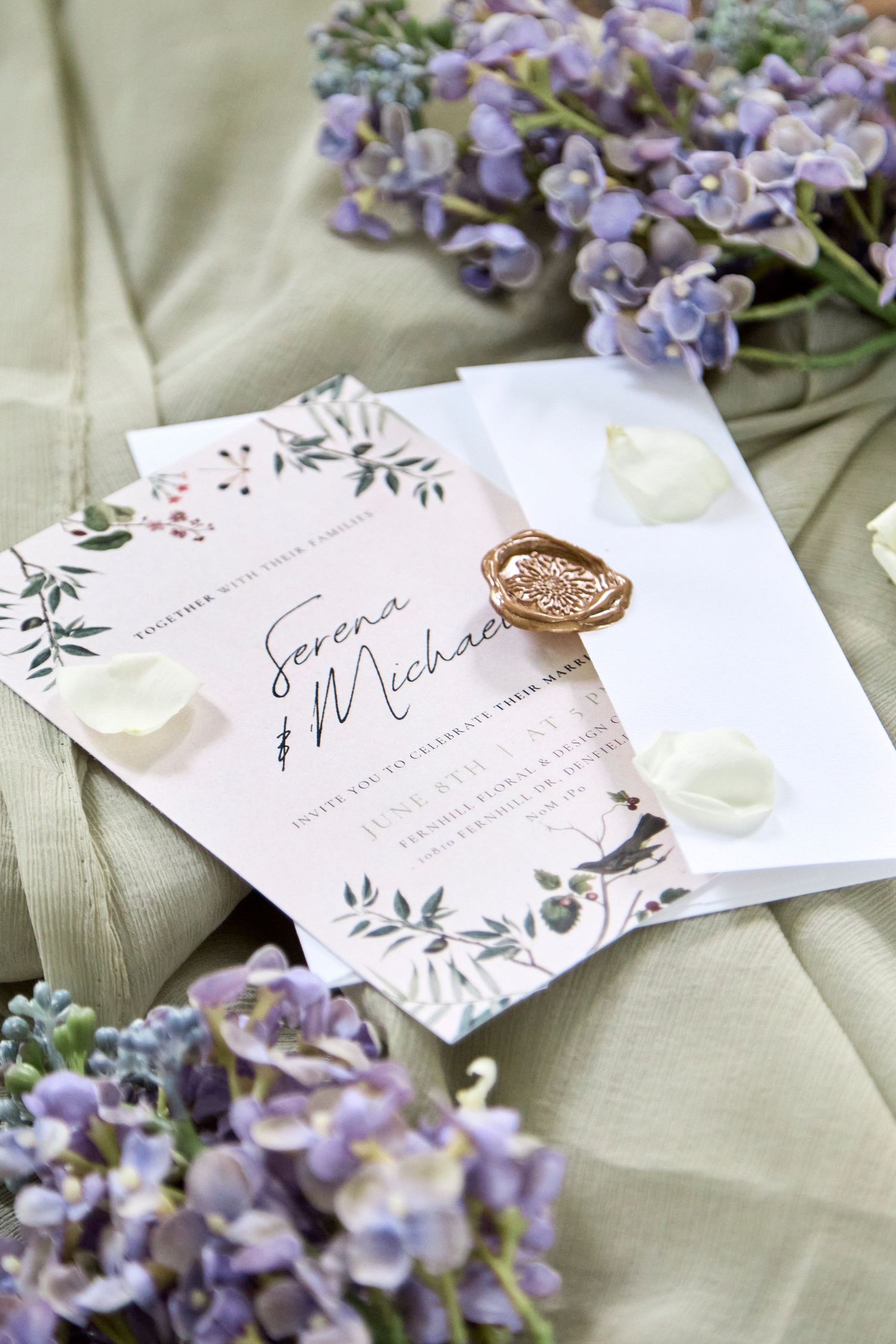 Layflat of wedding invitation with florals and green fabric.