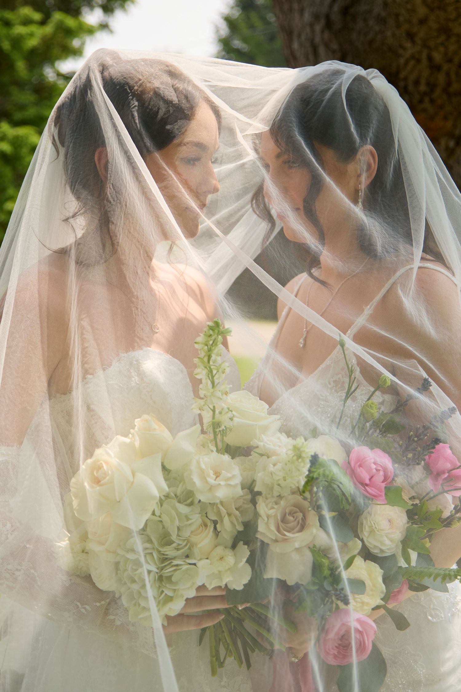 Bride and bride under veil with florals.