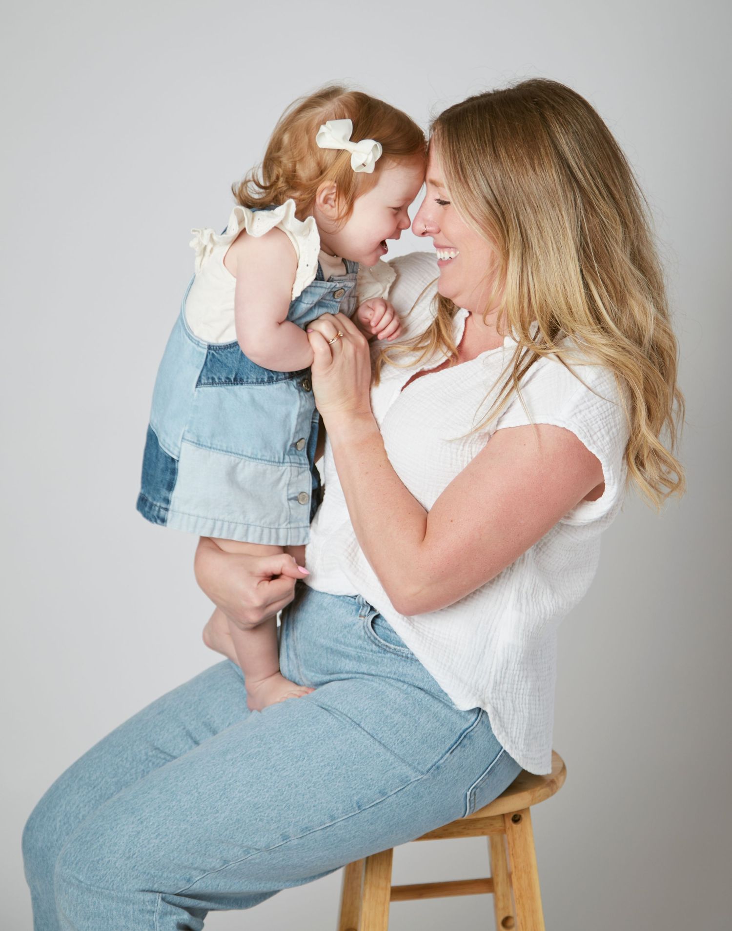 Mother and daughter in denim and white on grey background in studio.