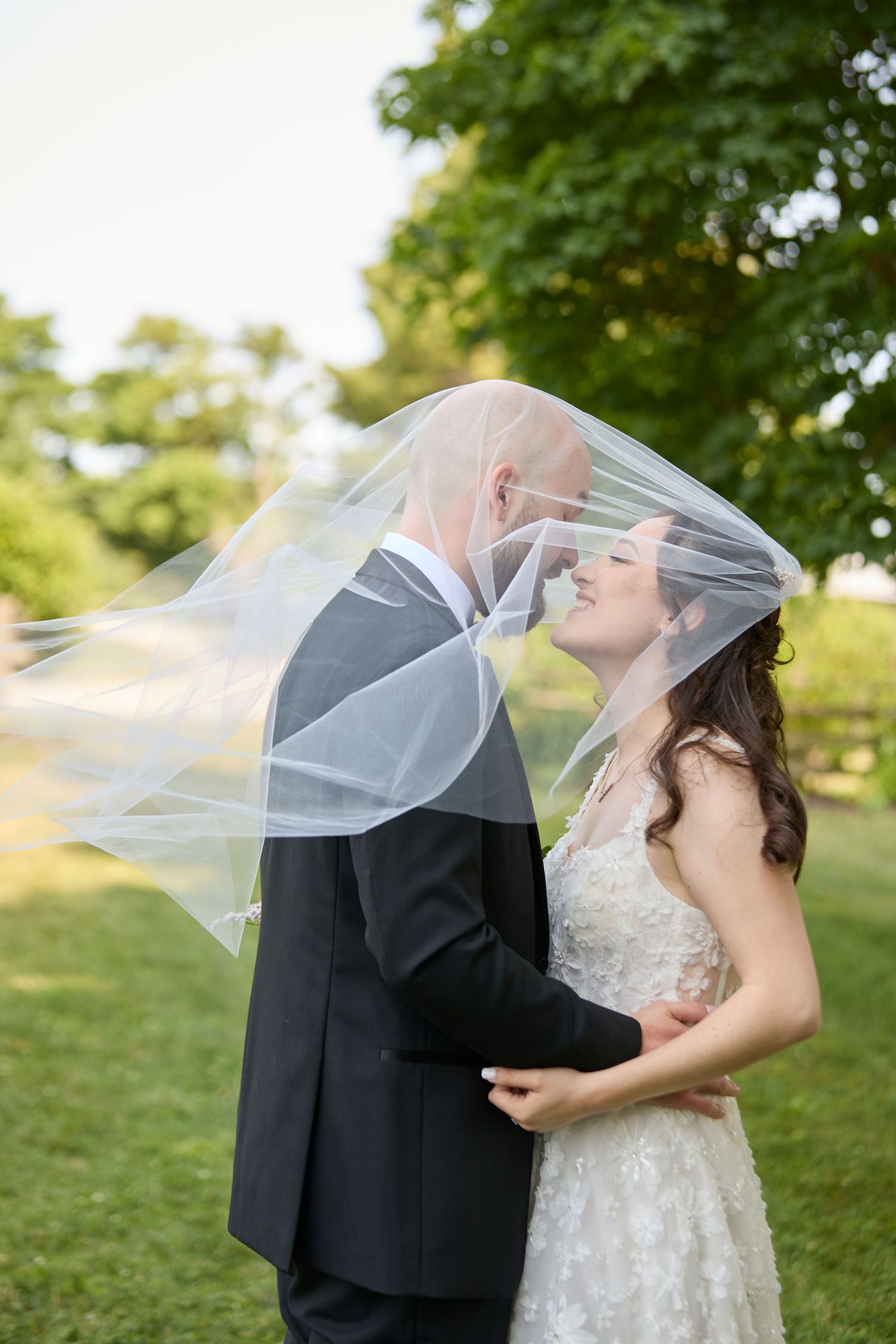 Bride and groom embrace with veil over heads.