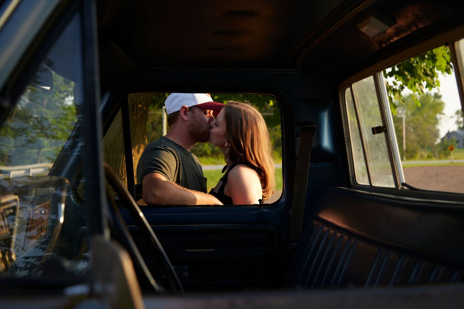 Couple kissing through window of vintage truck at golden hour.