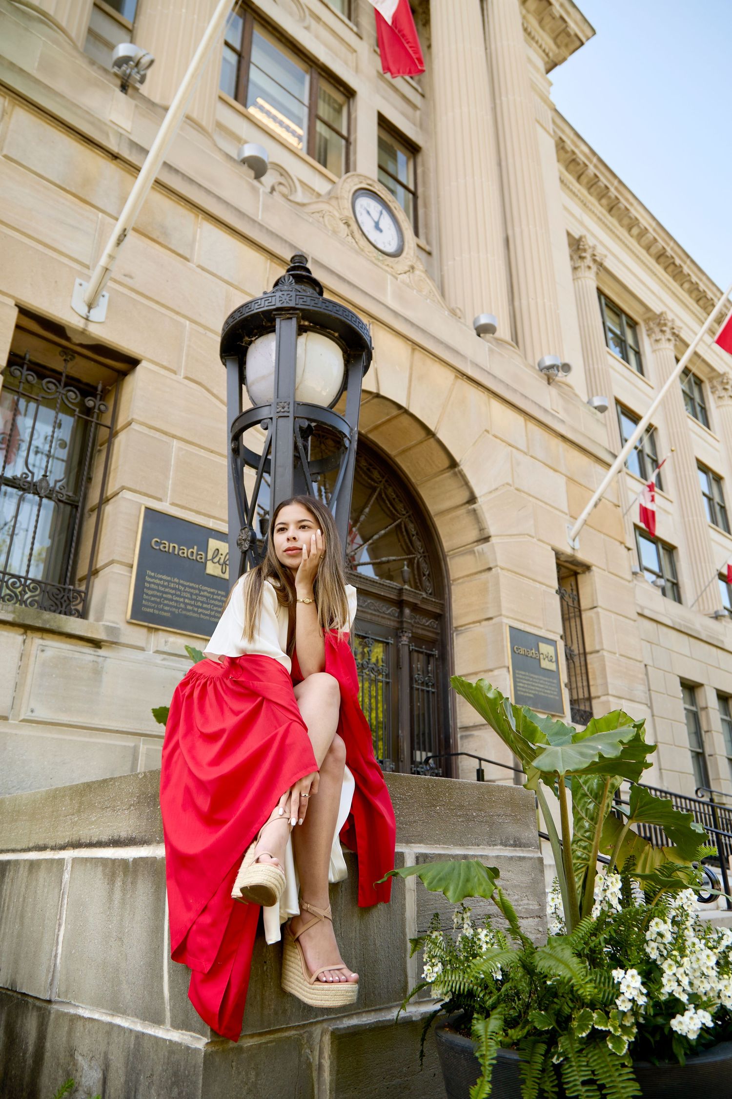 Grad photo of Fanshawe College student with red robe in front of Canada Life building.