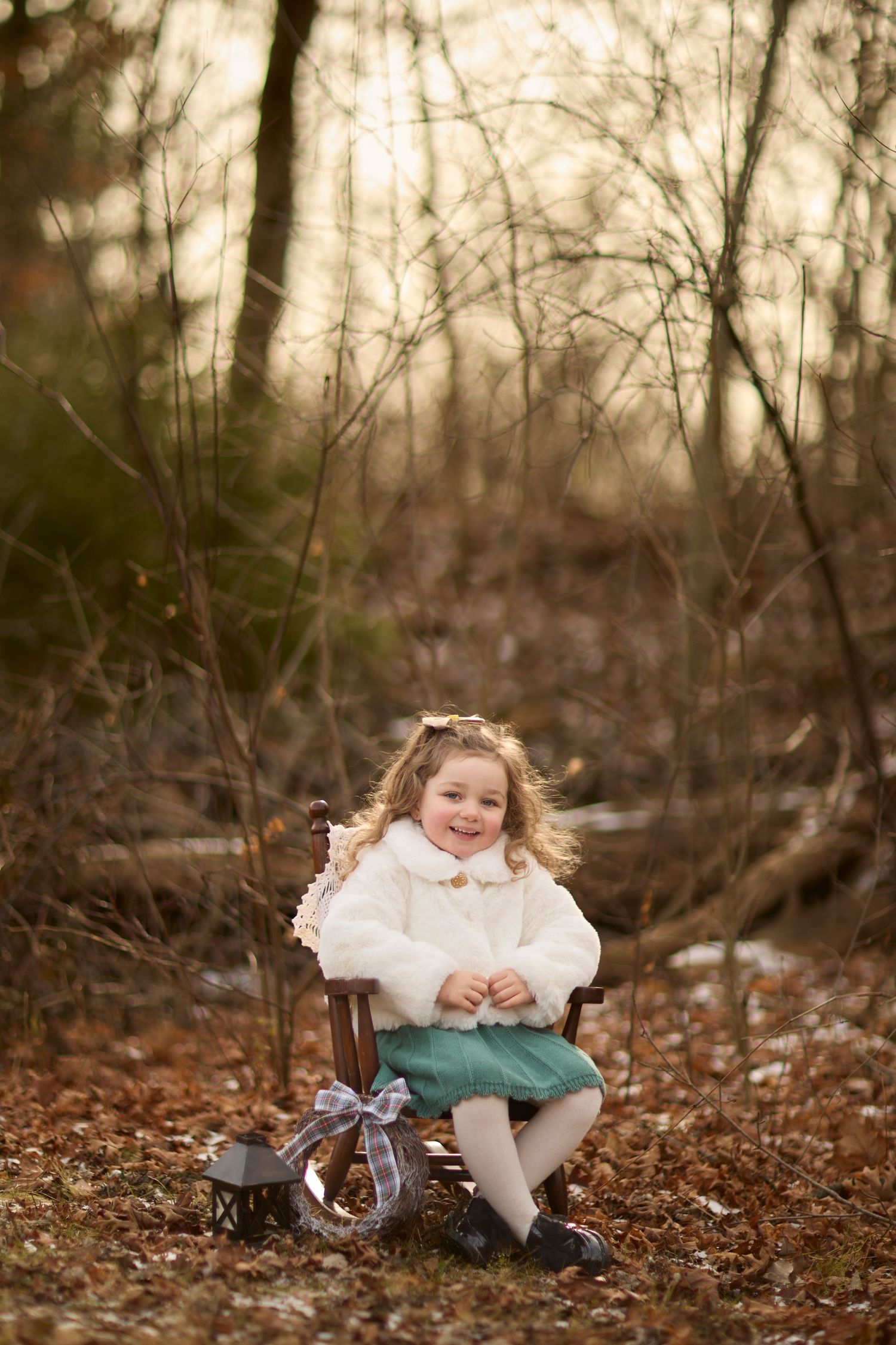 Christmas photo of girl in tiny rocking chair in a winter setting.