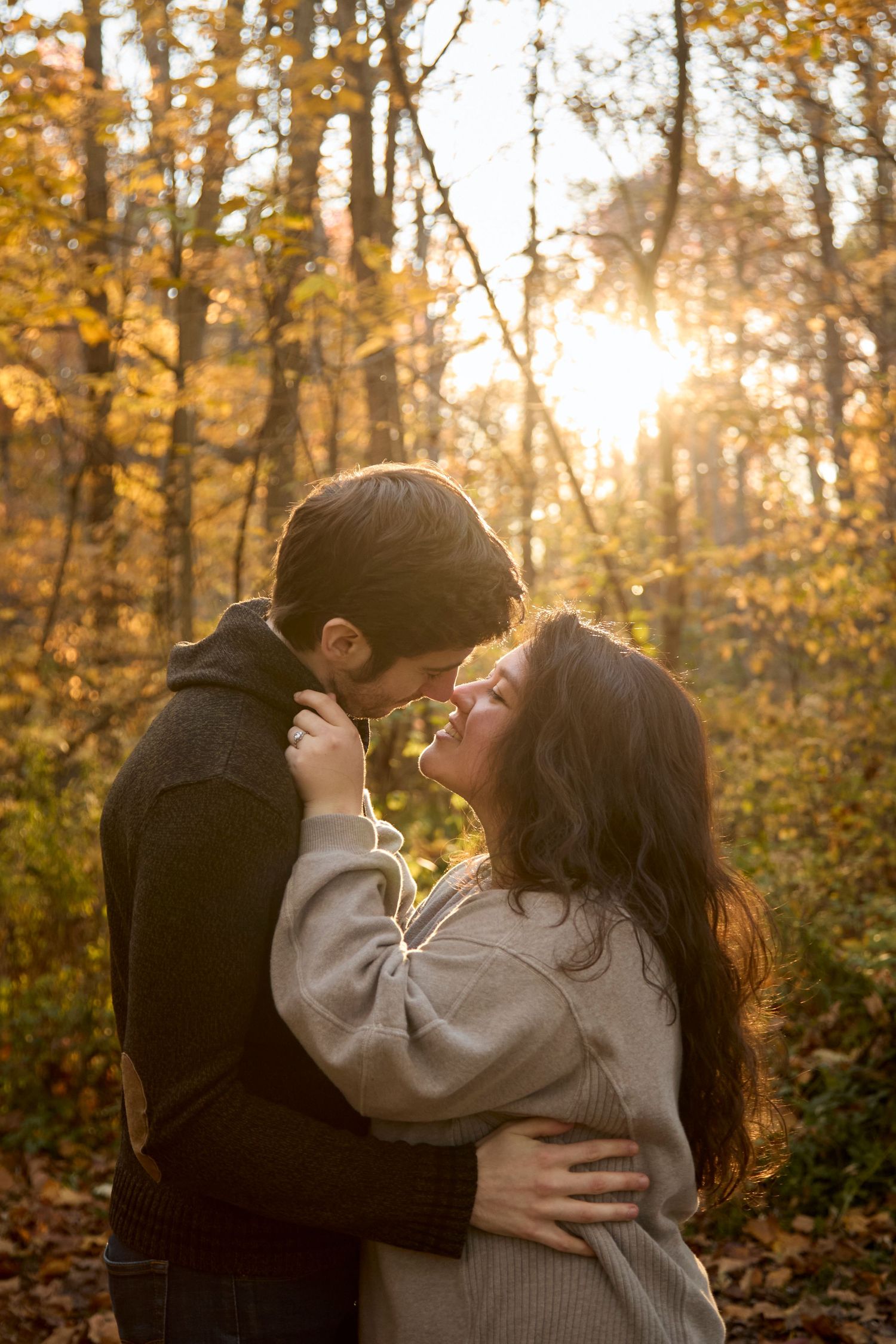 Couple embracing in woods at golden hour.