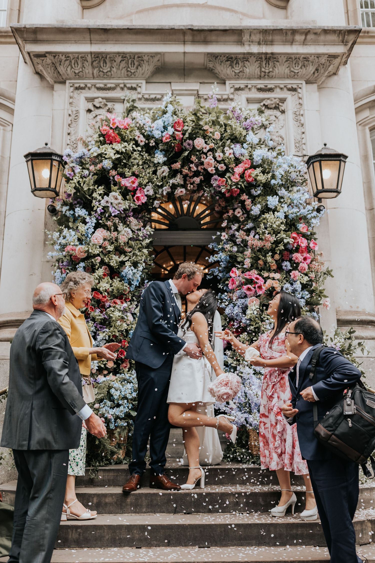 A couple getting married in front of a beautifully decorated floral arch on the steps of a grand building at Chelsea Old Town Hall