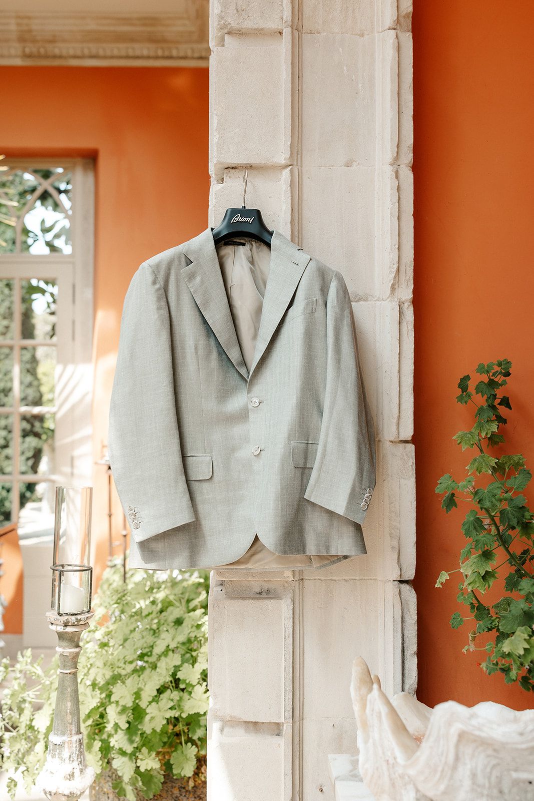 Light gray men's suit jacket hanging on a hanger against an orange wall with white stone architectural details.