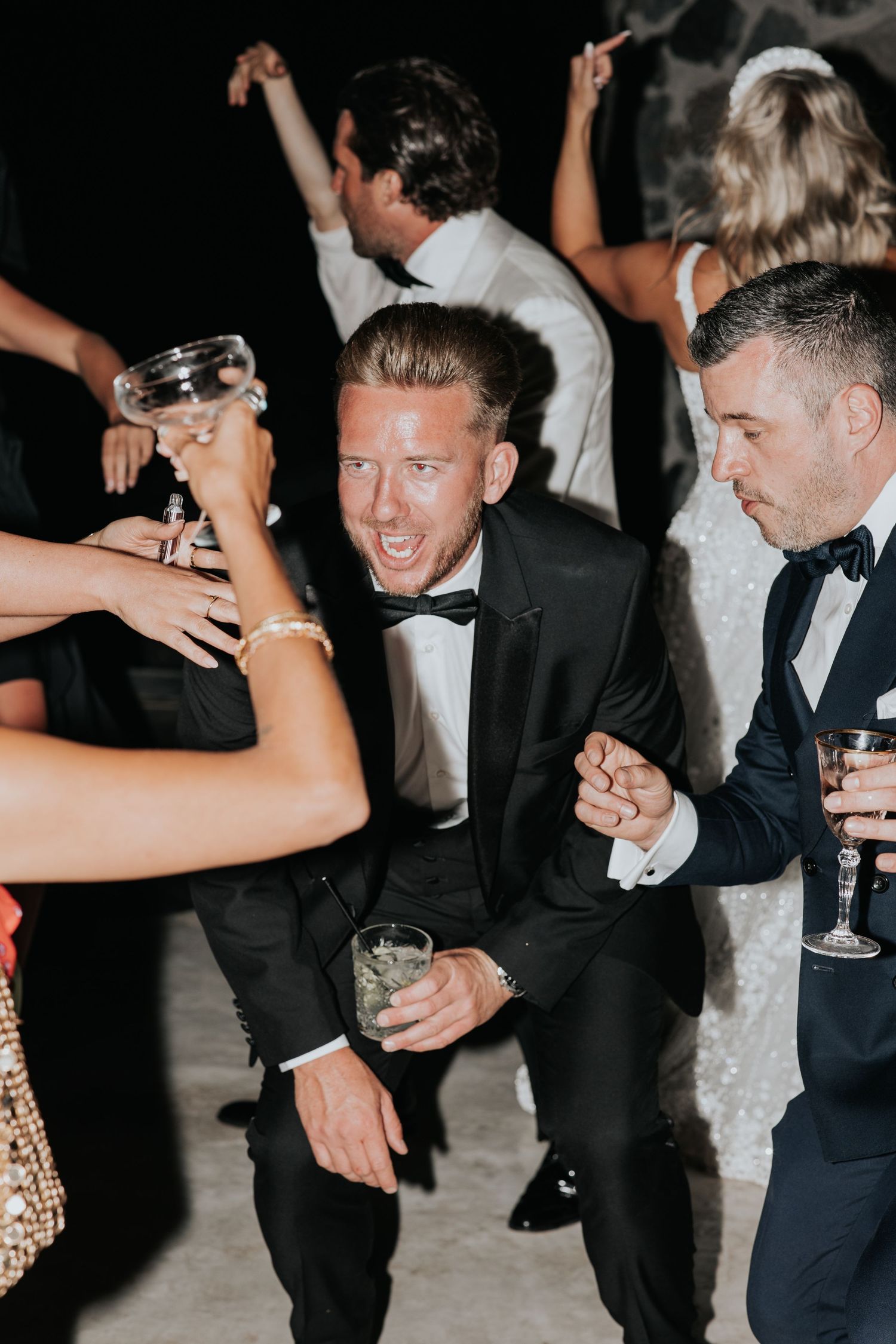 A group of well-dressed people enjoying a lively celebration, with one man enthusiastically raising his arms.