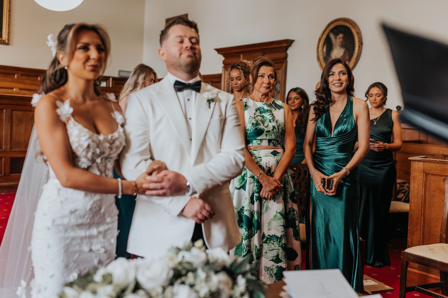 Bride and groom stand at the altar during wedding ceremony with emotional guests and bridesmaids in green dresses.