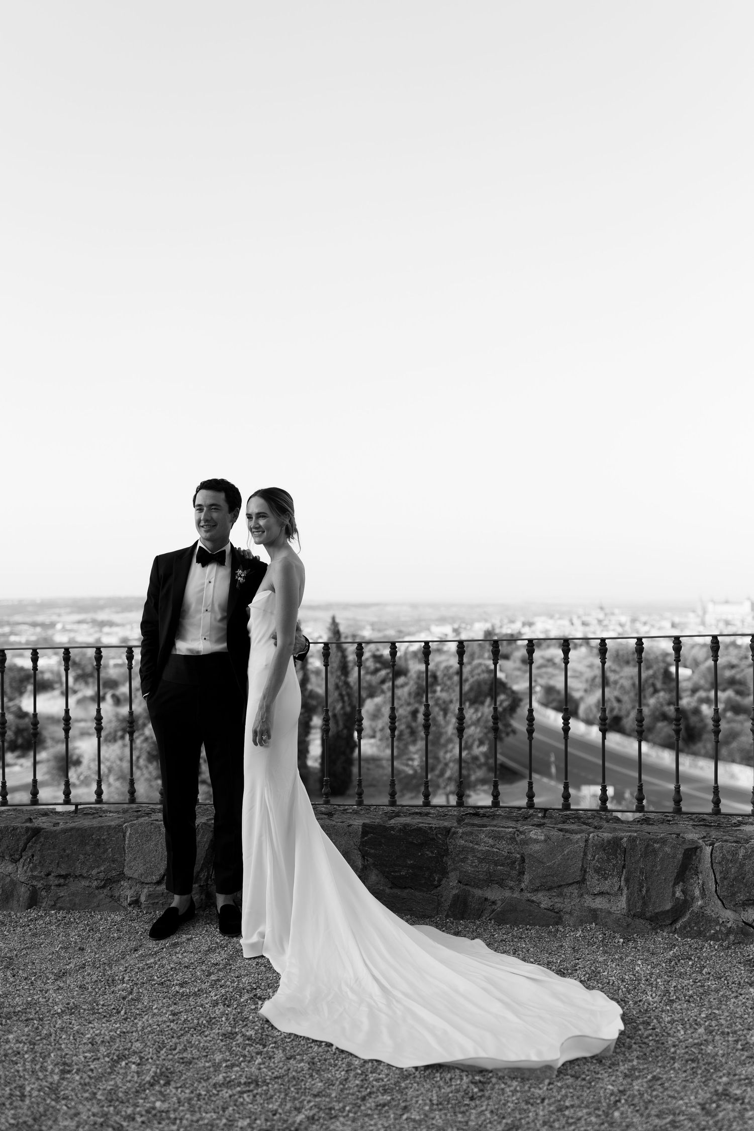 A black and white image of a bride and groom standing on a balcony overlooking a scenic landscape in Toledo