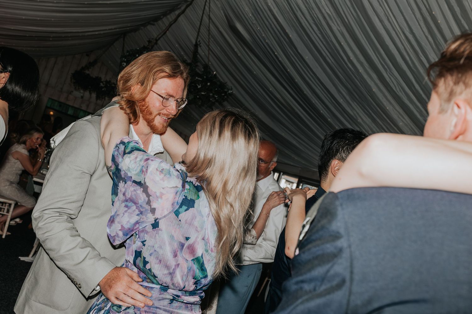Guests dancing and embracing at a wedding reception inside a tent venue.