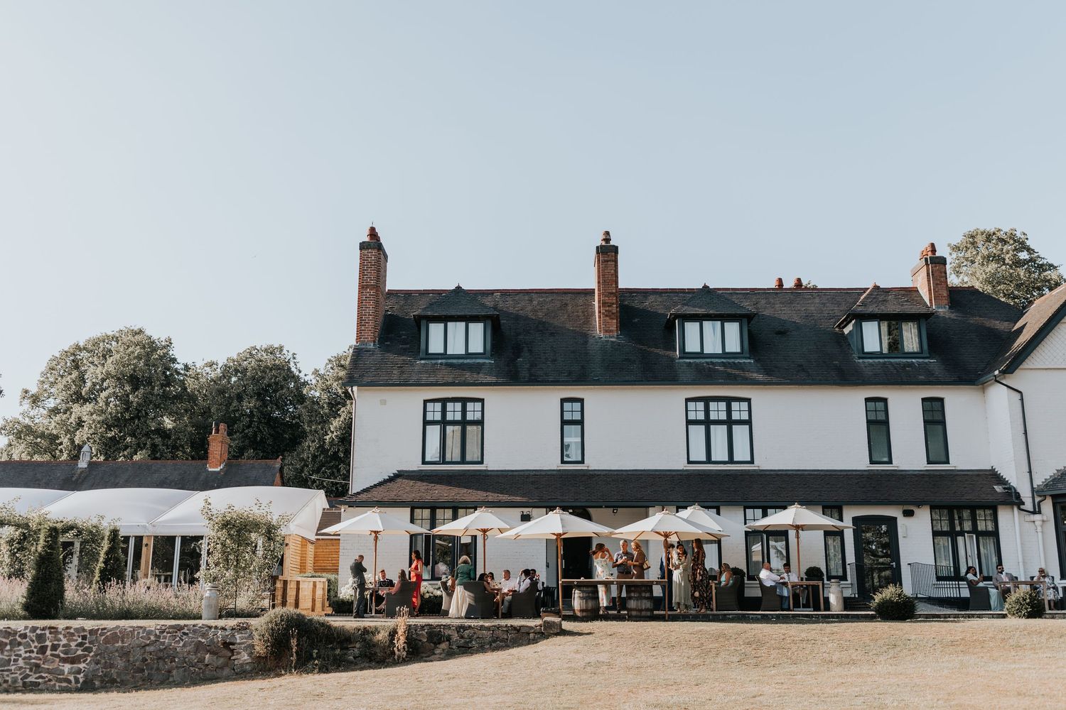 White country inn with outdoor seating, umbrellas, and guests dining al fresco on a sunny day.