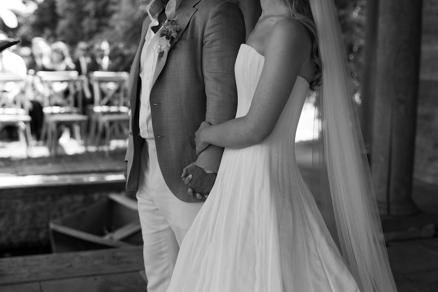Black and white photo of a bride and groom holding hands at their outdoor wedding ceremony.