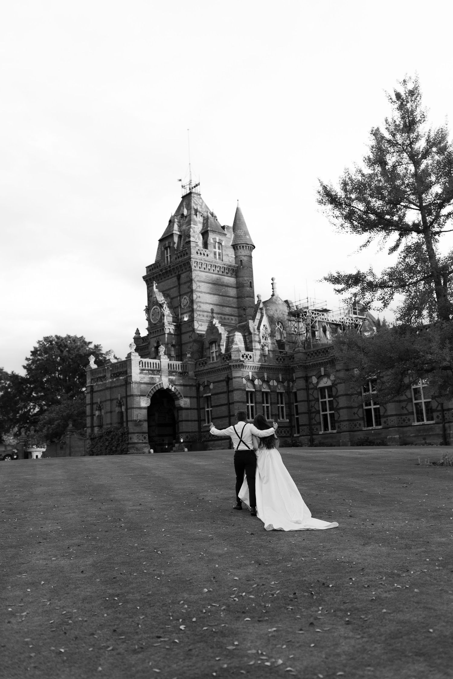 Black and white photo of a bride and groom walking toward a grand castle venue on their wedding day.