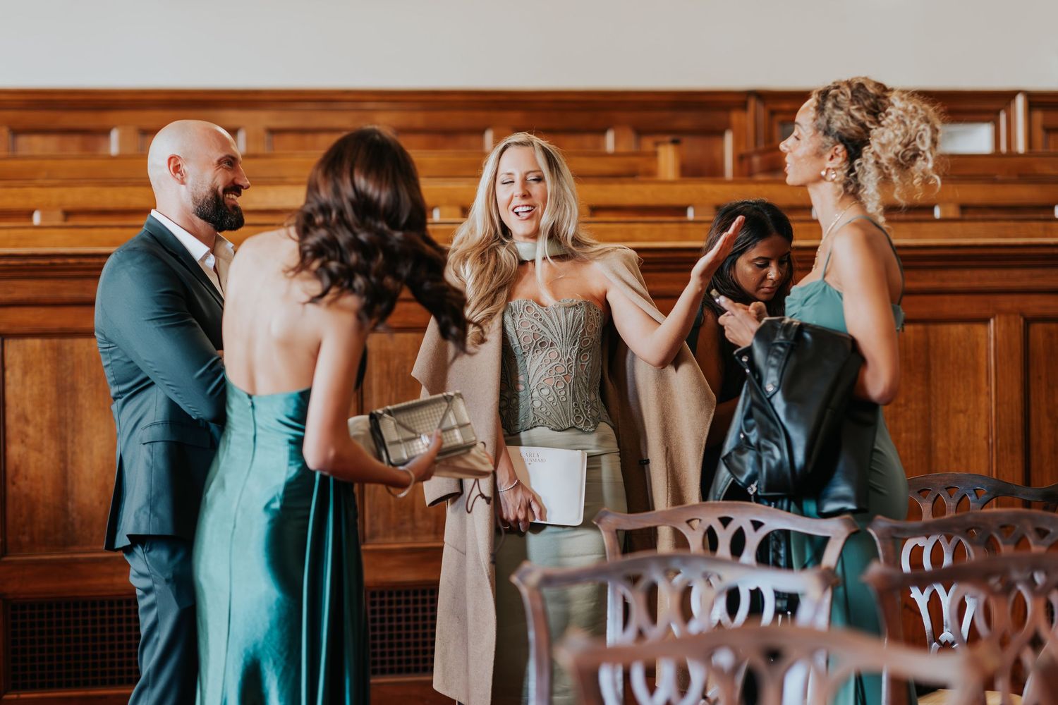Elegant wedding guests in teal gowns socializing in a wood-paneled venue during a formal celebration.