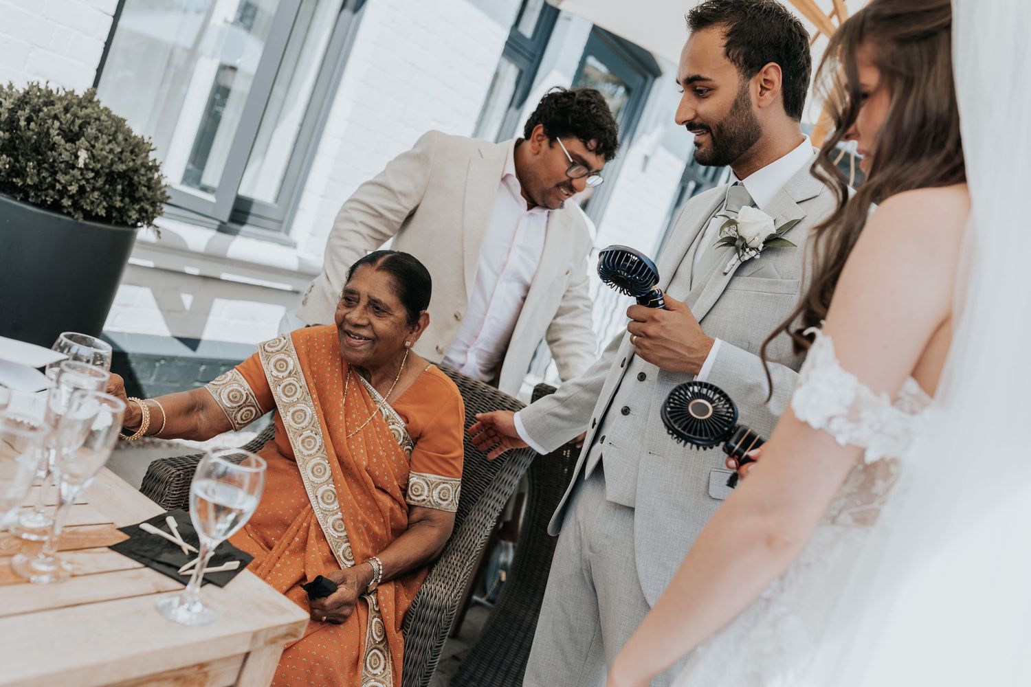 Wedding guests in elegant attire gather around a table, with bride in white gown greeting family members at reception.
