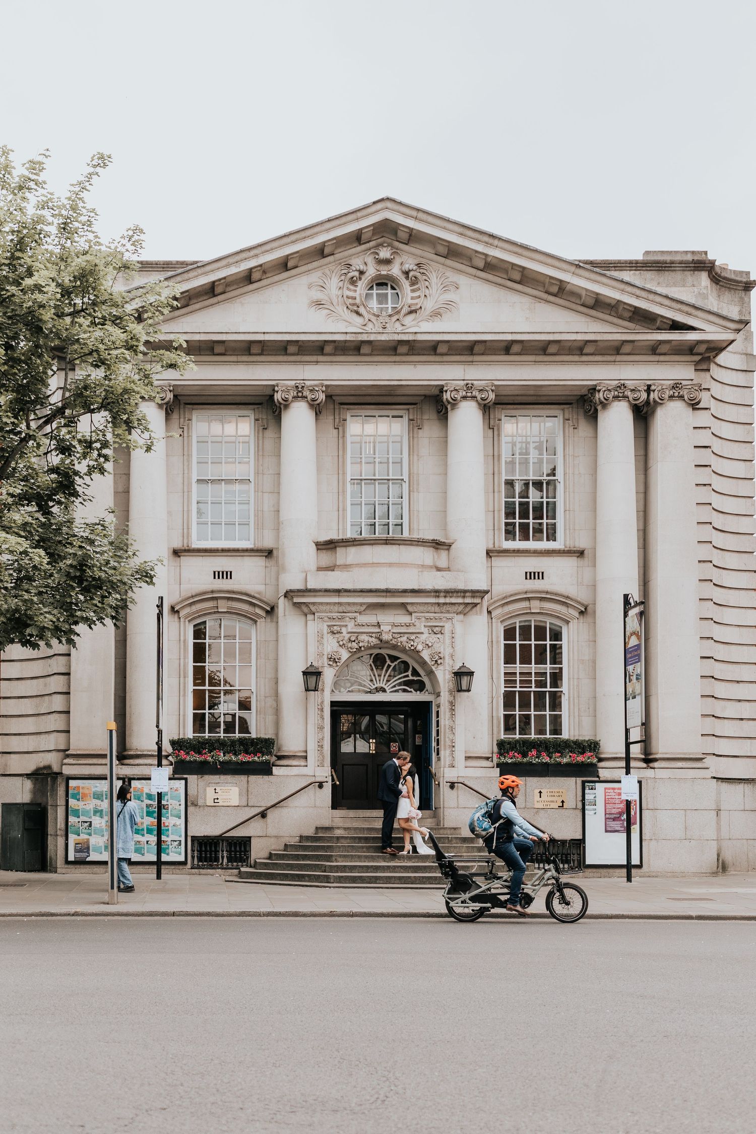 A grand, ornate building with a columned facade and decorative elements, with a person riding a bicycle in front of it.
