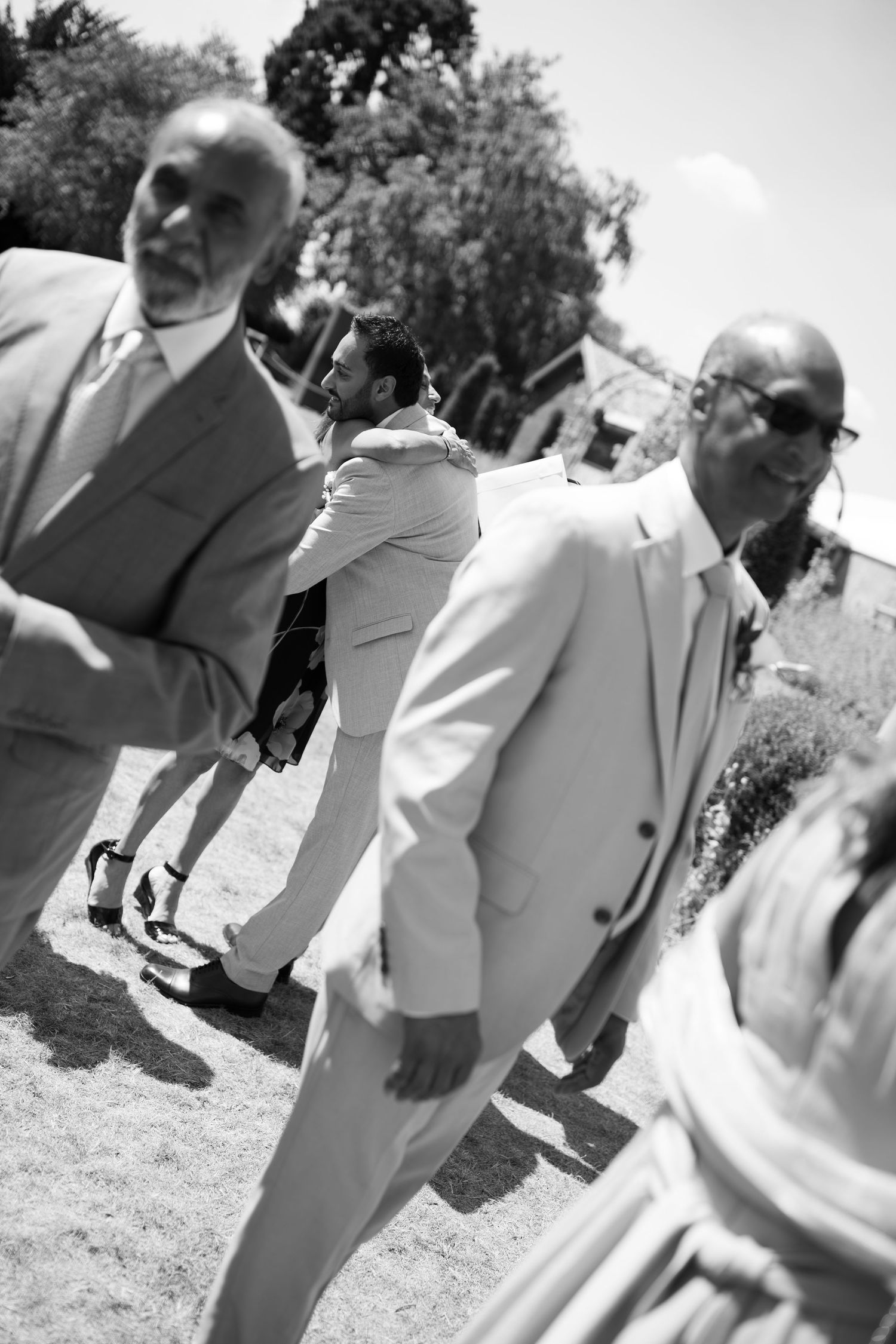 Black and white photo of men in suits walking outdoors at a formal event on a sunny day.