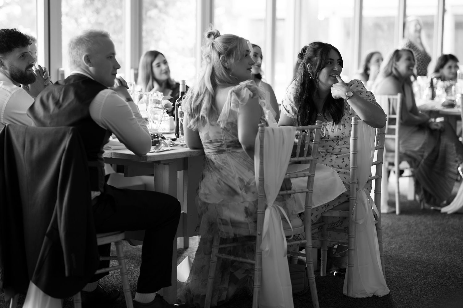 Black and white wedding reception photo of elegantly dressed guests seated at tables in a bright venue.