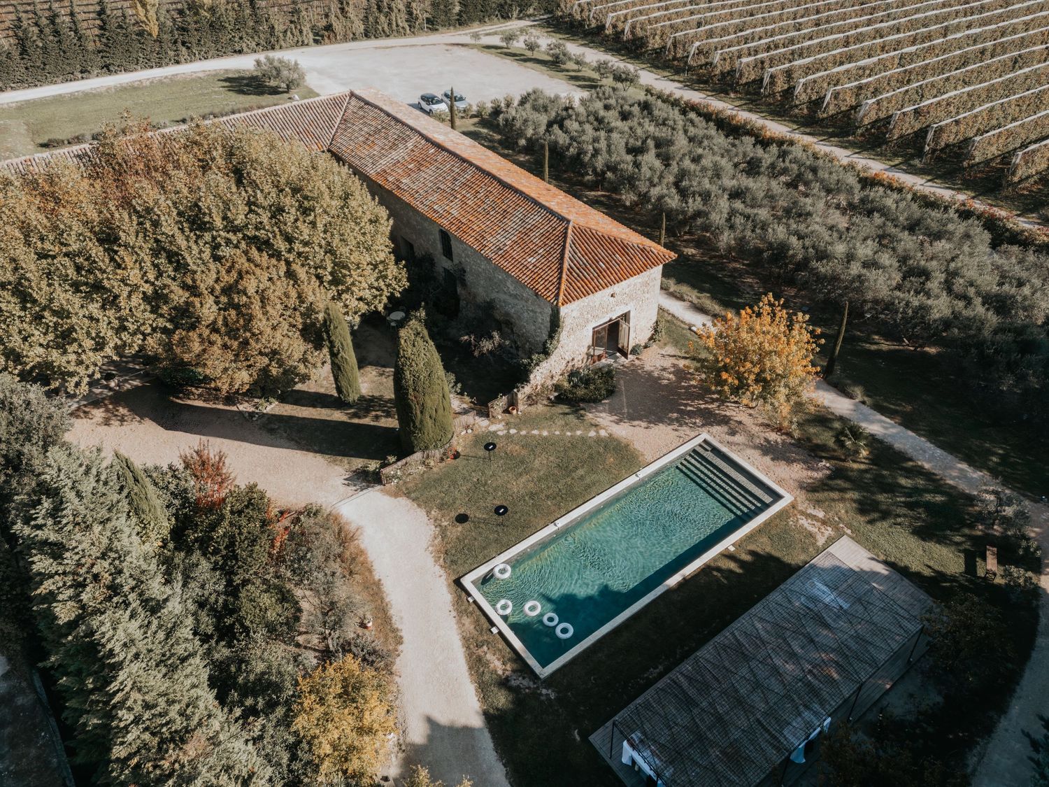 An aerial view of a winery with a large building, vineyards, and a swimming pool surrounded by lush greenery at Le Petit Roulet
