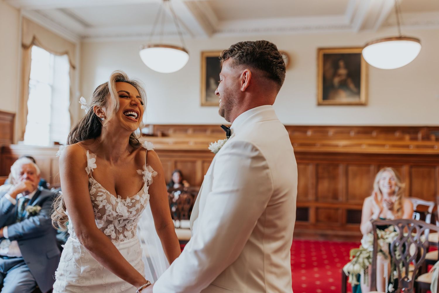 Bride and groom laughing together during wedding ceremony in elegant wood-paneled room.