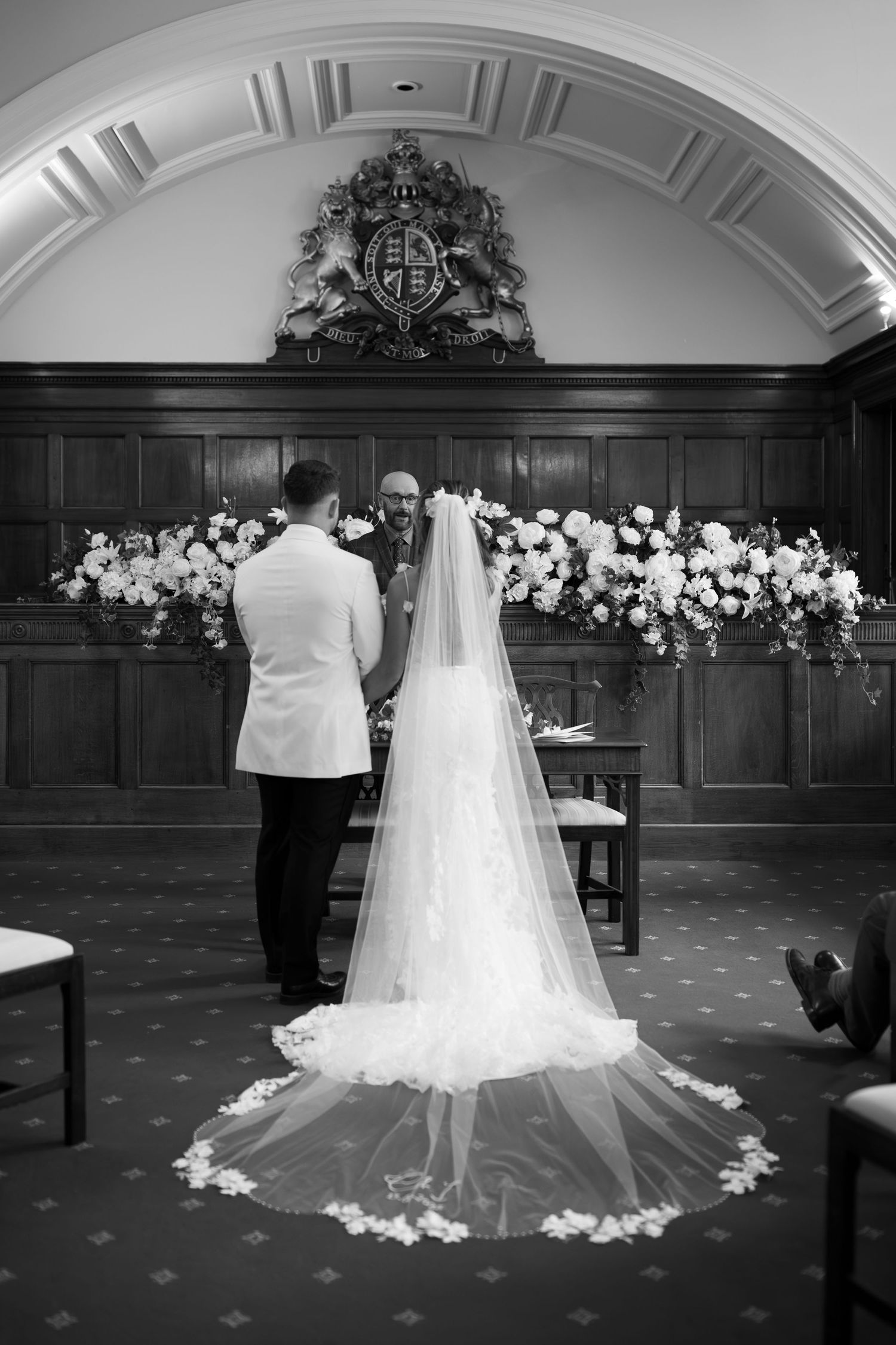 Black and white wedding ceremony photo showing bride in lace gown and veil at altar with groom and officiant.