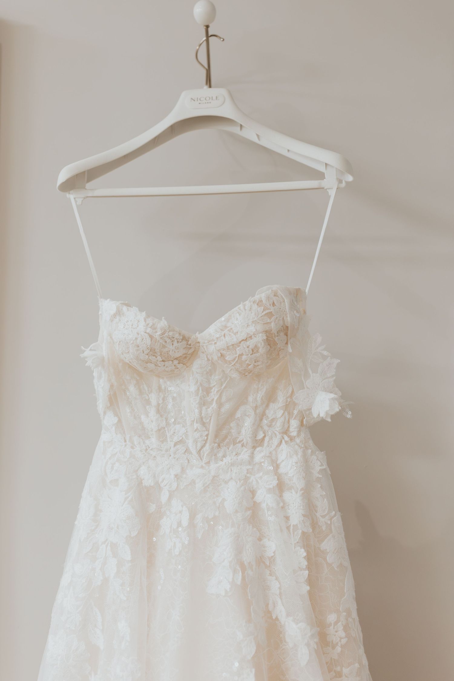 Elegant white lace strapless wedding dress with floral details hanging on a white hanger.