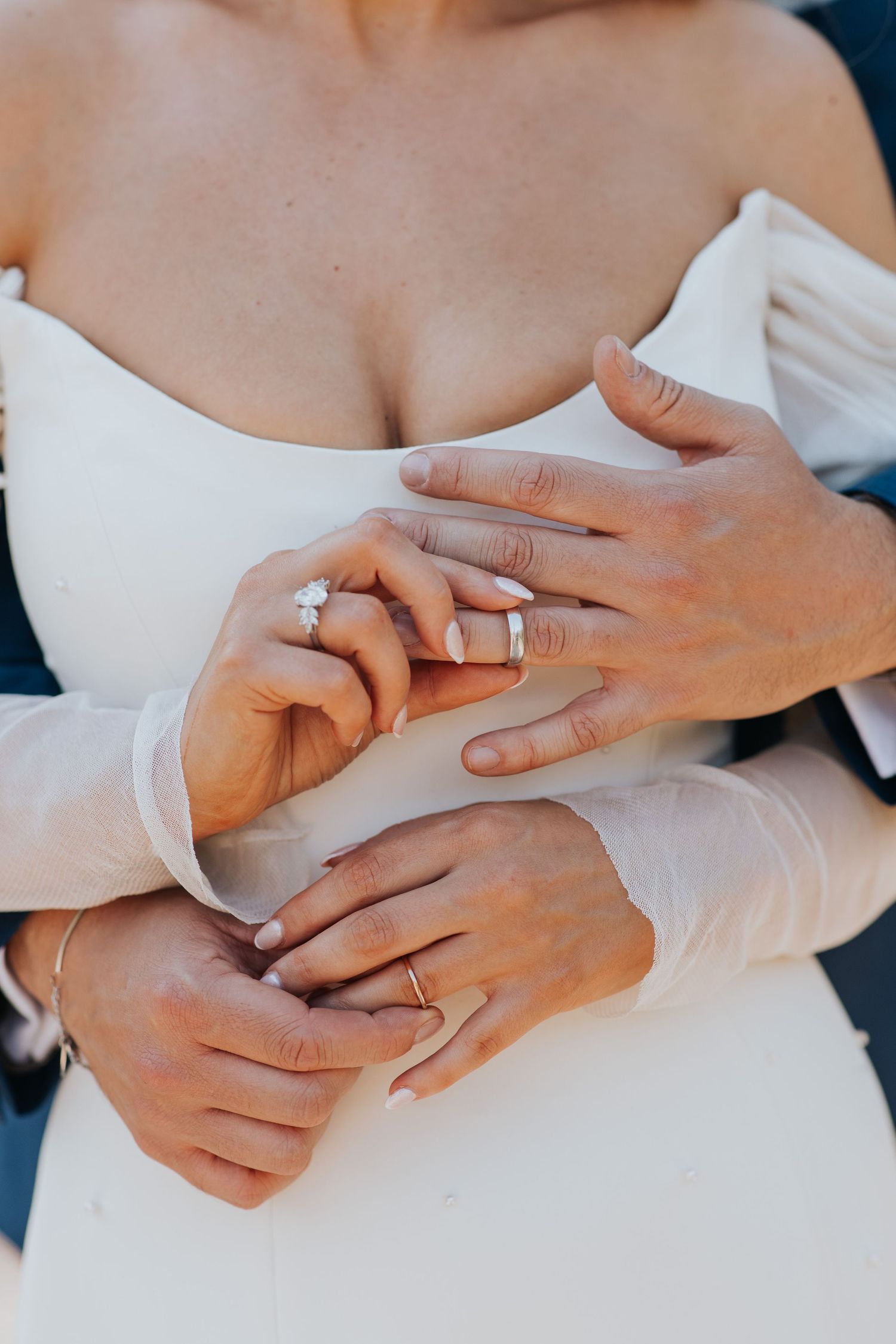 The image shows a close-up of a person's hands, with one hand wearing a ring, embracing another person's hand.
