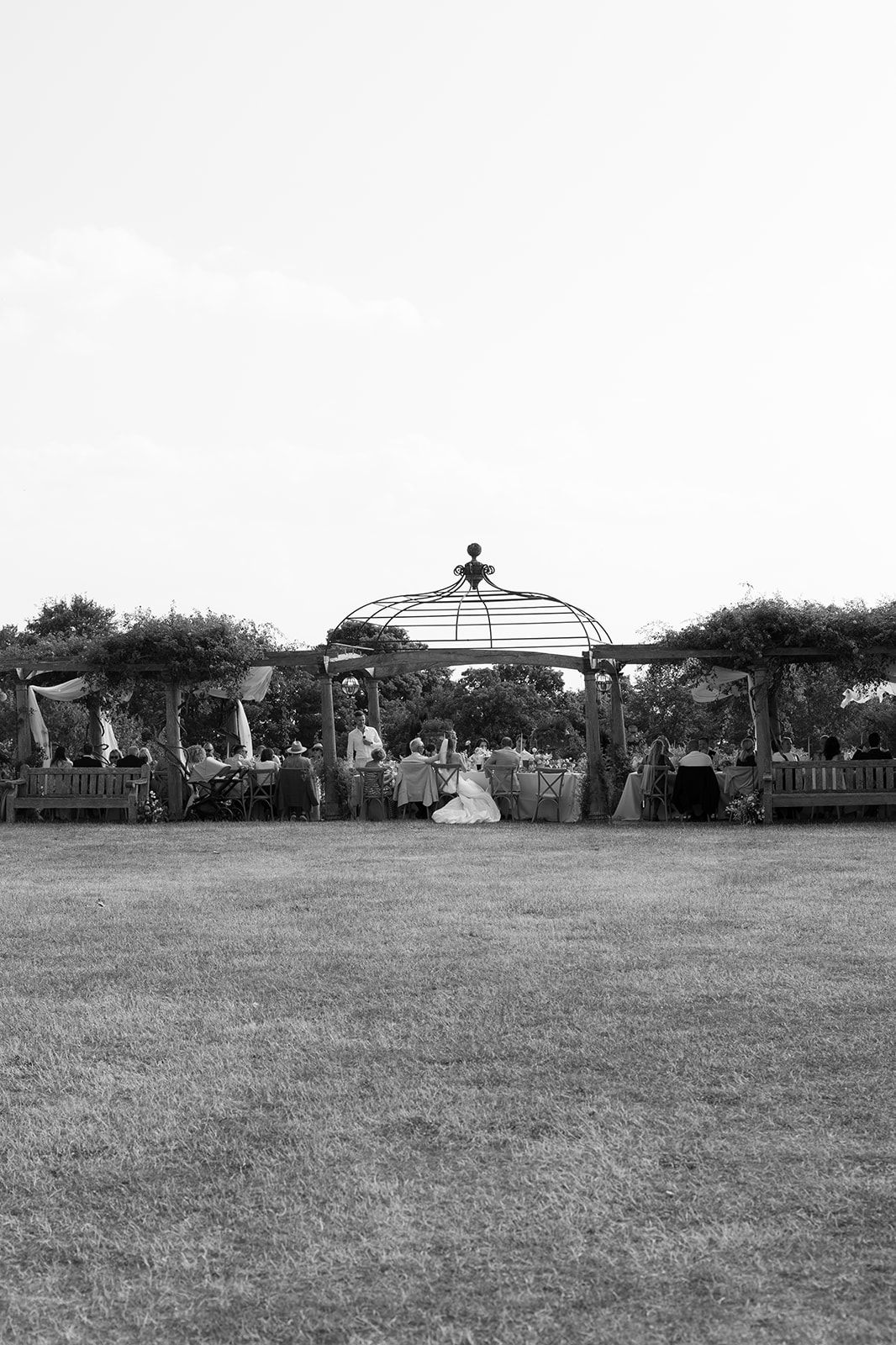 Black and white photo of an elegant outdoor wedding reception under a decorative gazebo.