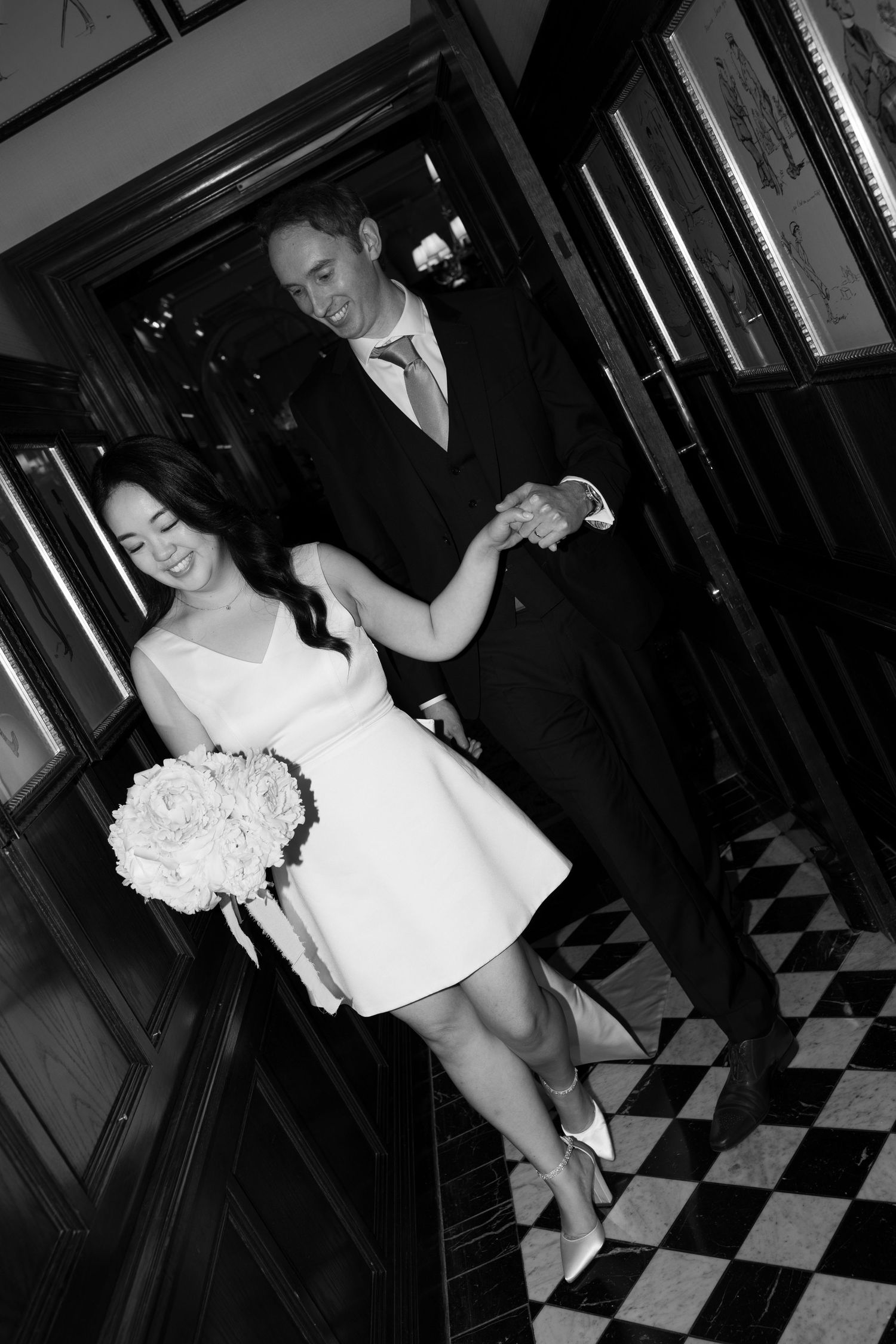 A black and white image shows a couple dressed formally dancing in what appears to be a hallway or entryway.