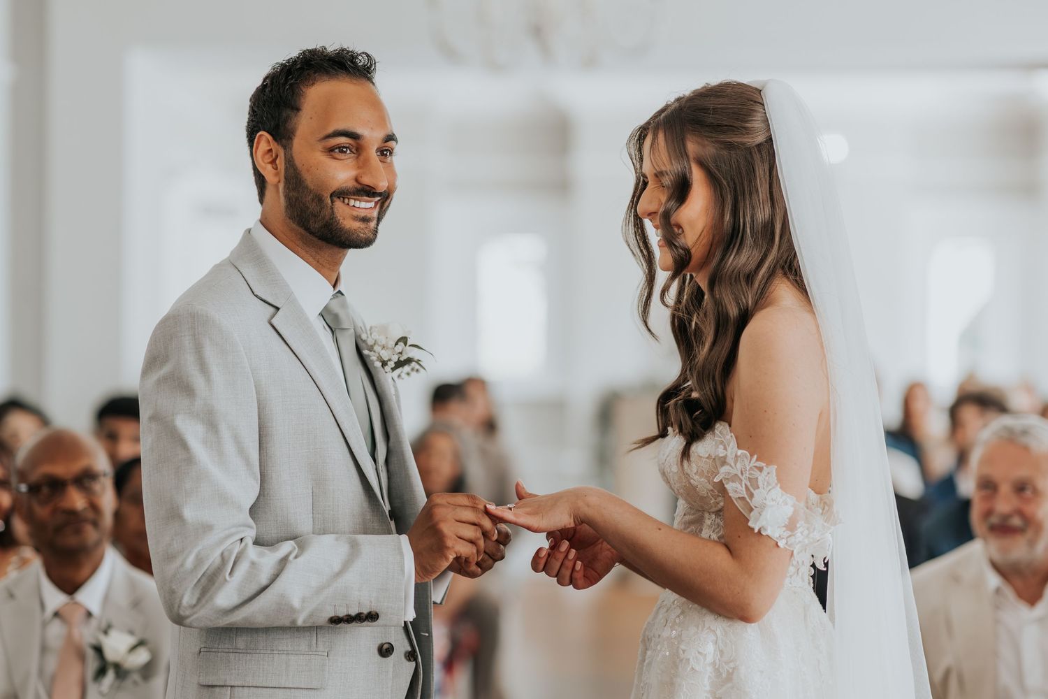 Bride and groom exchanging rings at a wedding ceremony, smiling joyfully in elegant attire.