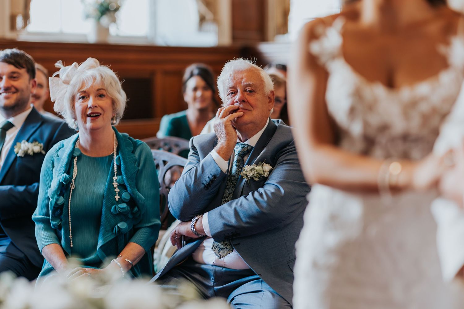 Joyful wedding guests laughing and smiling during a ceremony, seated in elegant wooden pews.