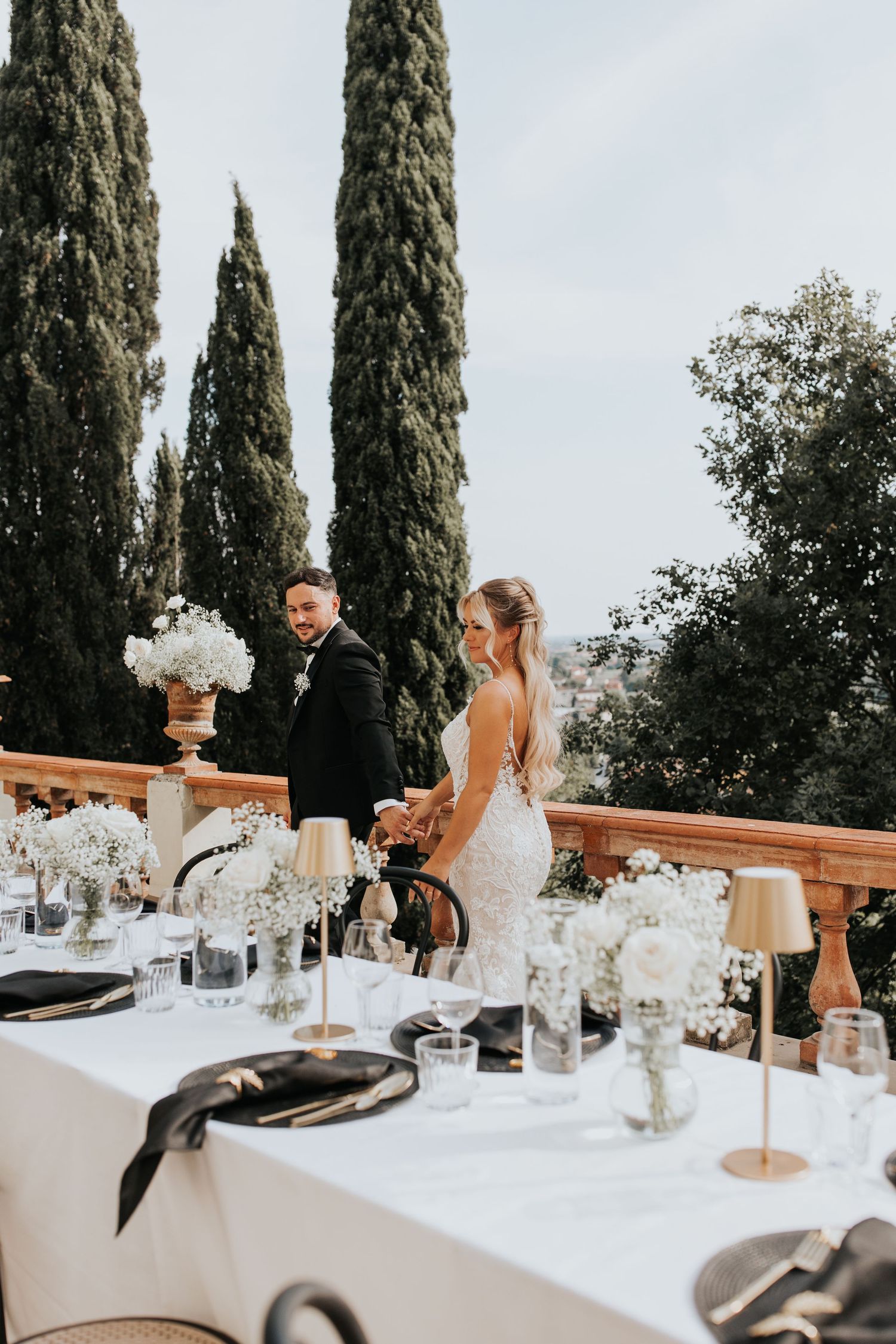 An elegant wedding reception with a beautifully set table, surrounded by lush greenery and cypress trees.