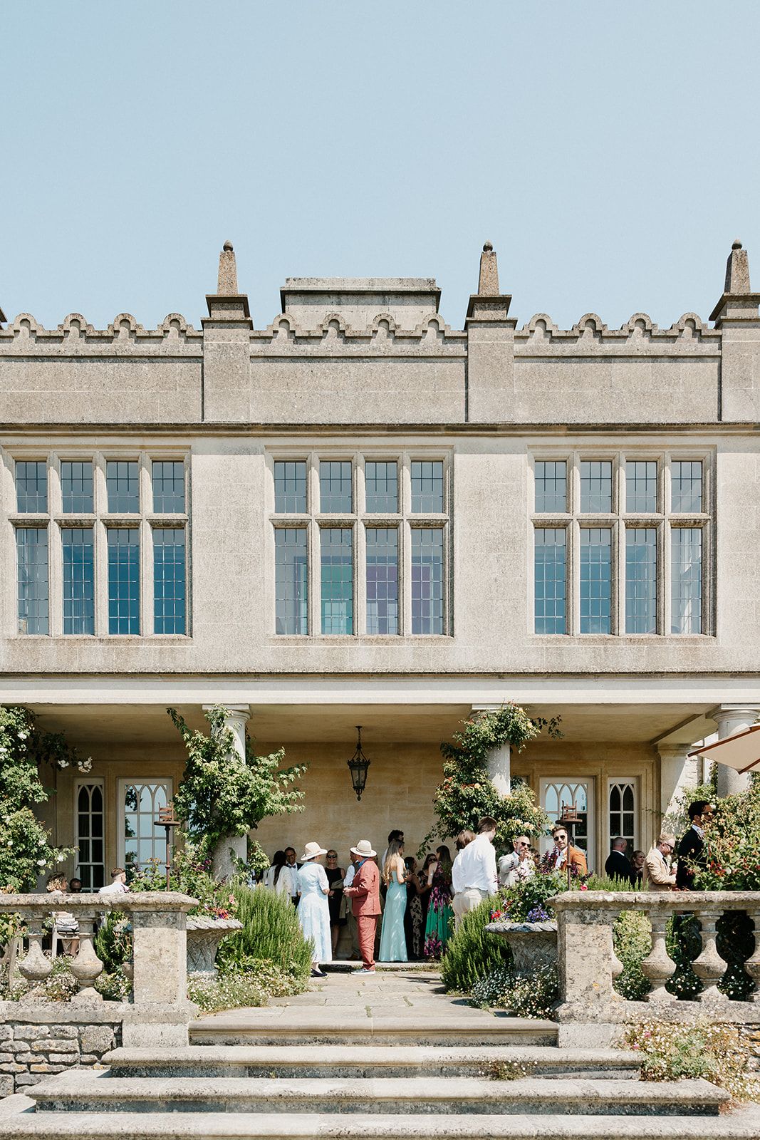 Elegant stone manor house wedding venue with guests gathered on the terrace on a sunny day.