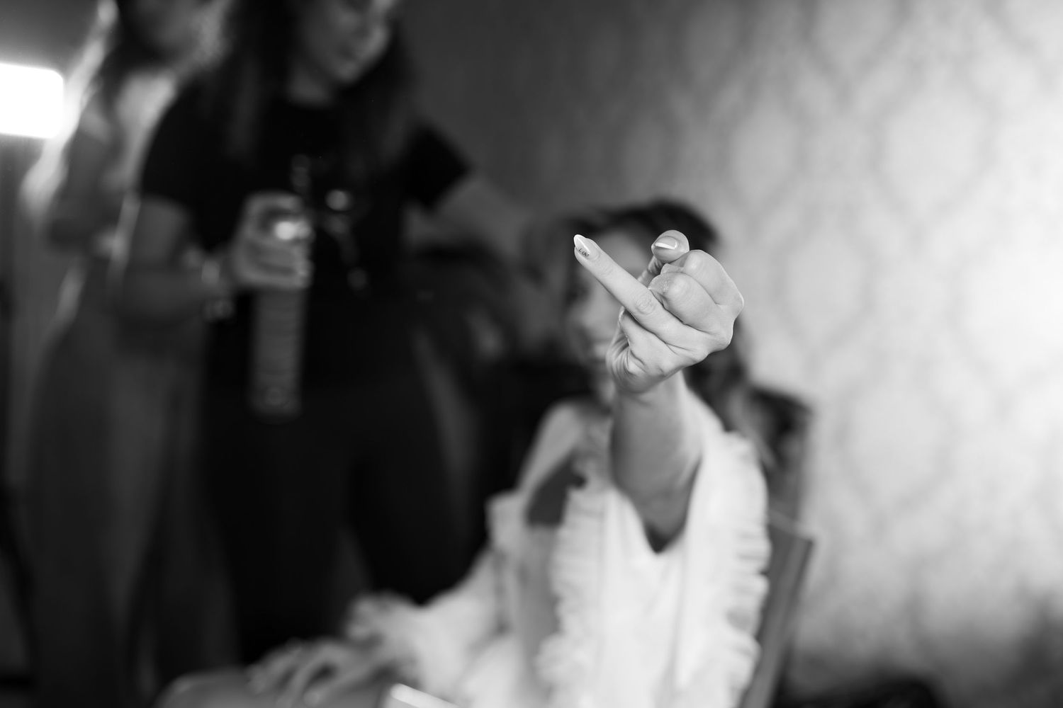 Black and white photo of a bride holding up her engagement ring while a stylist works in the background.